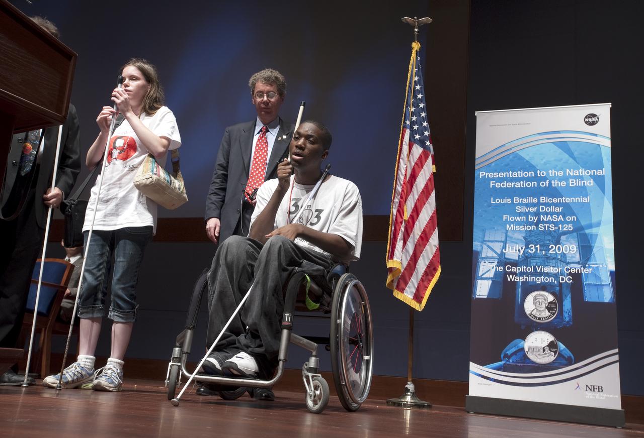 Derrick Tuff, right in wheelchair, and Kayla Weathers, standing left,  deliver  remarks at a ceremony where senior NASA officials presented the National Federation of the Blind with two Louis Braille Bicentennial Silver Dollars that flew on Space Shuttle Atlantis' mission (STS-125) to the Hubble Space Telescope in May 2009, Friday evening, July 31, 2009, at the Capitol Visitors Center in Washington. Man standing at center is unidentified. Photo Credit: (NASA/Paul E. Alers)