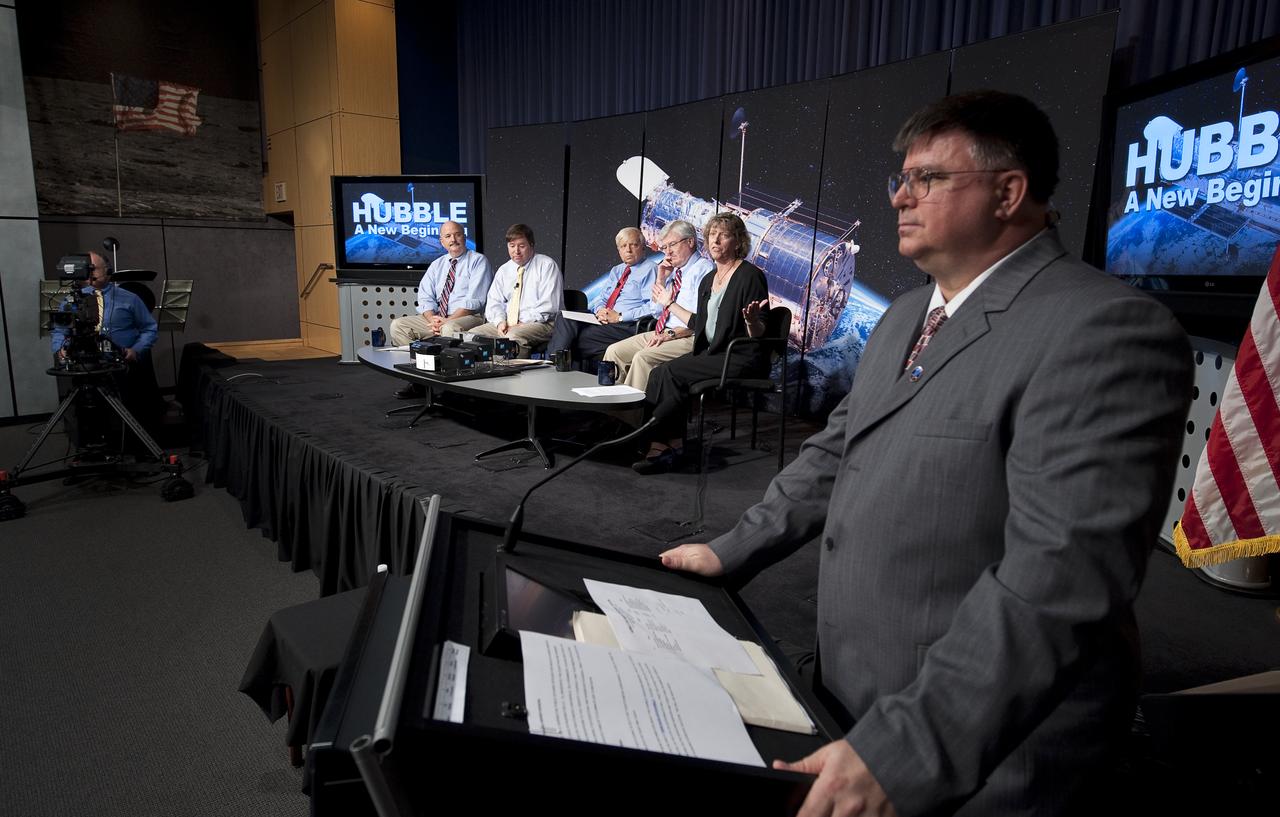 NASA Public Affairs Officer J.D. Harrington, left, monitors a press conference where NASA released images from NASA's Hubble Space Telescope Wednesday, Sept. 9, 2009 at NASA Headquarters in Washington. Participants on stage from left, Bob O'Connell, chair of the science oversight committee for the NASA Hubble Space Telescope Wide Field Camera 3, James Green, the Cosmic Origins Spectrograph principal investigator, NASA Associate Administrator of the Science Mission Directorate Dr. Edward J. Weiler, David Leckrone, senior project scientist, and Heidi Hammel, senior research scientist at the Space Science Institute in Boulder.  The images were from four of the telescopes' six operating science instruments. Photo Credit: (NASA/Bill Ingalls)