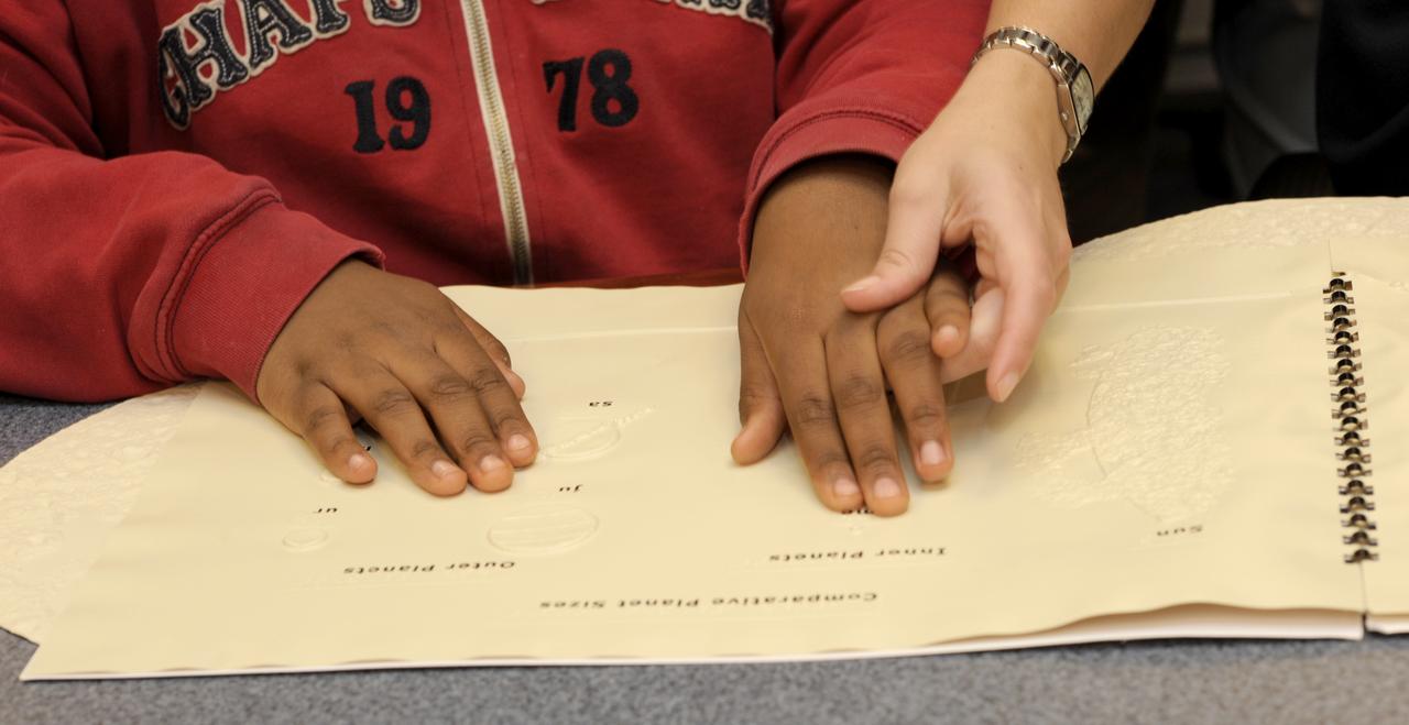 The hands of Maryland School for the Blind student Andrea Washington, are guided across a topographical map of the Solar System by science teacher Colleen Shovestull during a visit to NASA Headquarters in Washington, Thursday, Oct. 29, 2009.  Seven students from the Maryland School for the Blind visited NASA and participated in activities to learn about NASA'smission, functions, and careers. Photo Credit: (NASA/Paul E. Alers)