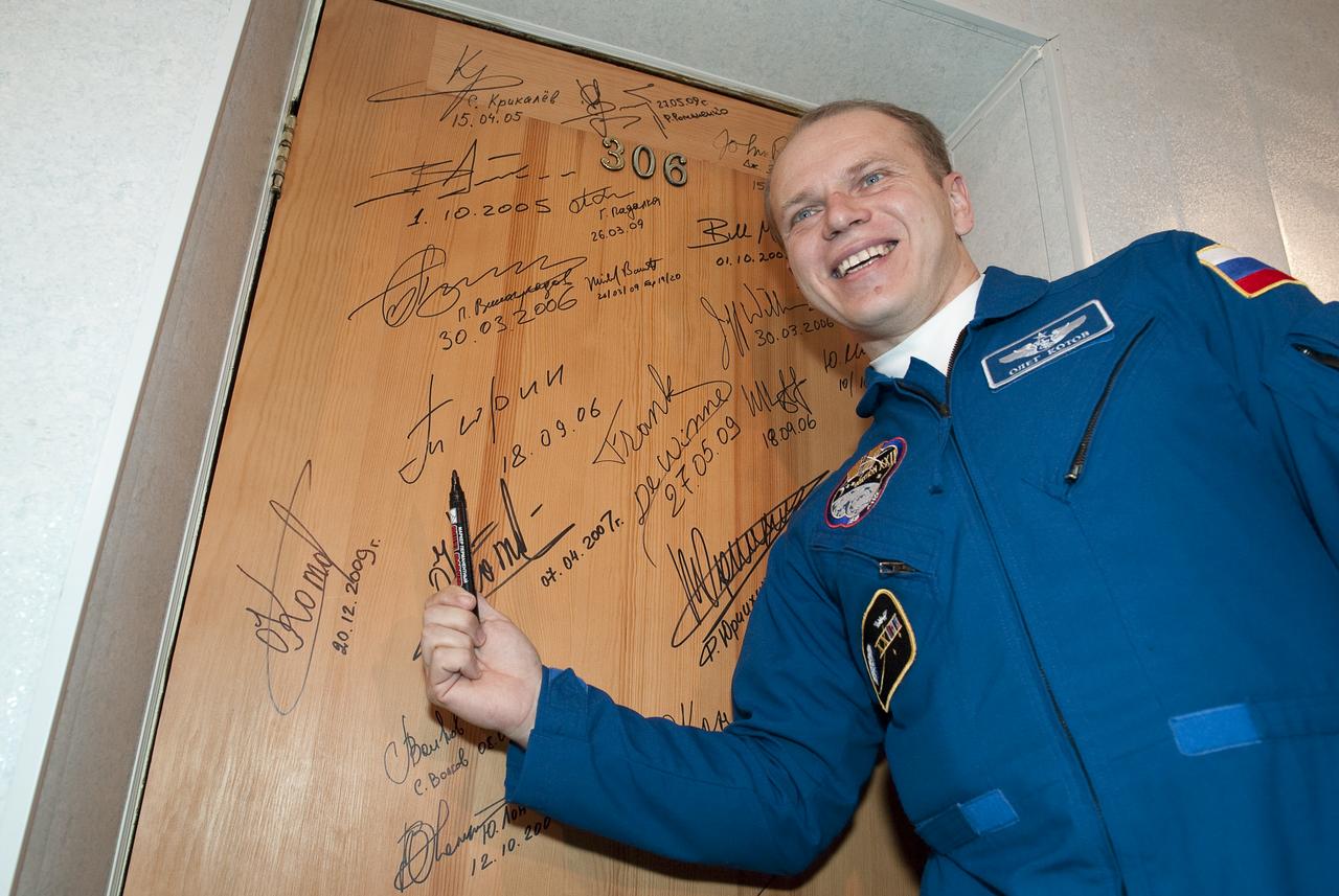 Expedition 22 Soyuz Commander Oleg Kotov of Russia smiles for photographers after performing the traditional door signing at the Cosmonaut Hotel in Baikonur, Kazakhstan before departing with fellow crew members, NASA Flight Engineer Timothy J. Creamer of the U.S., and Flight Engineer Soichi Noguchi of Japan to suit up for their launch, Sunday, Dec. 20, 2009.   Photo Credit: (NASA/Bill Ingalls)