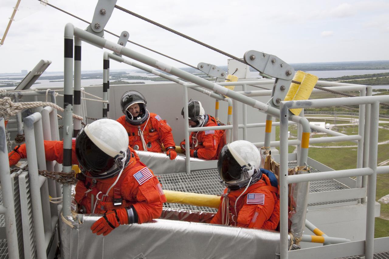 CAPE CANAVERAL, Fla. - On Launch Pad 39A at NASA's Kennedy Space Center, STS-132 Mission Specialists Garrett Reisman, left, and Michael Good, dressed in their orange launch-and-entry suits, position themselves inside the slidewire basket, at front, as they practice emergency exit procedures at the pad. In the slidewire basket, in back, are Mission Specialists Piers Sellers, left, and Steve Bowen.  Evacuation from the pad's 195-foot level in the event of an emergency is made possible by seven baskets suspended from seven slidewires that extend from the fixed service structure to a landing zone 1,200 feet west of the pad.  The crew is participating in a launch dress rehearsal, called the Terminal Countdown Demonstration Test, or TCDT.  TCDT provides each shuttle crew and launch team the opportunity to participate in various simulated countdown activities, including equipment familiarization and emergency procedures.  On the STS-132 mission, the six-member crew will deliver an Integrated Cargo Carrier, or ICC, and the Russian-built Mini-Research Module-1, or MRM-1, to the International Space Station aboard space shuttle Atlantis.  The ICC is an unpressurized flat bed pallet and keel yoke assembly used to support the transfer of exterior cargo from the shuttle to the space station.  The MRM-1, known as Rassvet, is the second in a series of new pressurized components for Russia and will be permanently attached to the Earth-facing port of the Zarya control module. Rassvet, which translates to 'dawn,' will be used for cargo storage and will provide an additional docking port to the station.  STS-132 is the 34th mission to the station and the 132nd shuttle mission overall.   Atlantis is targeted to launch on May 14 at 2:19 p.m.  For information on the STS-132 mission, visit http:__www.nasa.gov_mission_pages_shuttle_shuttlemissions_sts132_index.html. Photo credit: NASA_Jack Pfaller