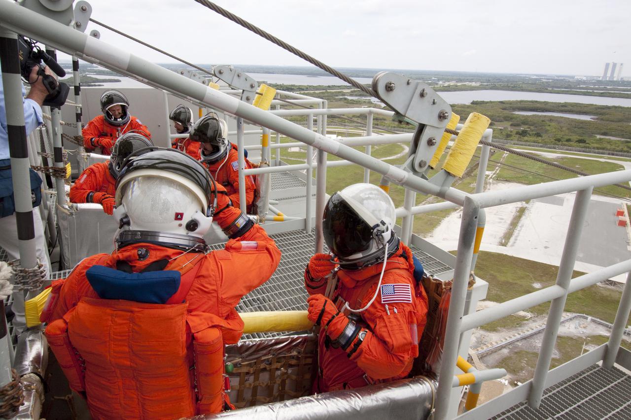CAPE CANAVERAL, Fla. - At Launch Pad 39A at NASA's Kennedy Space Center in Florida, STS-132 Commander Ken Ham, left, and Pilot Tony Antonelli, dressed in their orange launch-and-entry suits, position themselves in the slidewire basket, in front, as they practice emergency exit procedures at the pad. In the center basket are Mission Specialists Garrett Reisman, left, and Michael Good.  In the slidewire basket in the back are Mission Specialists Piers Sellers, left, and Steve Bowen.  Evacuation from the pad's 195-foot level in the event of an emergency is made possible by seven baskets suspended from seven slidewires that extend from the fixed service structure to a landing zone 1,200 feet west of the pad.  The crew is participating in a launch dress rehearsal, called the Terminal Countdown Demonstration Test, or TCDT.  TCDT provides each shuttle crew and launch team the opportunity to participate in various simulated countdown activities, including equipment familiarization and emergency procedures.  On the STS-132 mission, the six-member crew will deliver an Integrated Cargo Carrier, or ICC, and the Russian-built Mini-Research Module-1, or MRM-1, to the International Space Station aboard space shuttle Atlantis.  The ICC is an unpressurized flat bed pallet and keel yoke assembly used to support the transfer of exterior cargo from the shuttle to the space station.  The MRM-1, known as Rassvet, is the second in a series of new pressurized components for Russia and will be permanently attached to the Earth-facing port of the Zarya control module. Rassvet, which translates to 'dawn,' will be used for cargo storage and will provide an additional docking port to the station.  STS-132 is the 34th mission to the station and the 132nd shuttle mission overall.   Atlantis is targeted to launch on May 14 at 2:19 p.m.  For information on the STS-132 mission, visit http:__www.nasa.gov_mission_pages_shuttle_shuttlemissions_sts132_index.html. Photo credit: NASA_Jack Pfaller