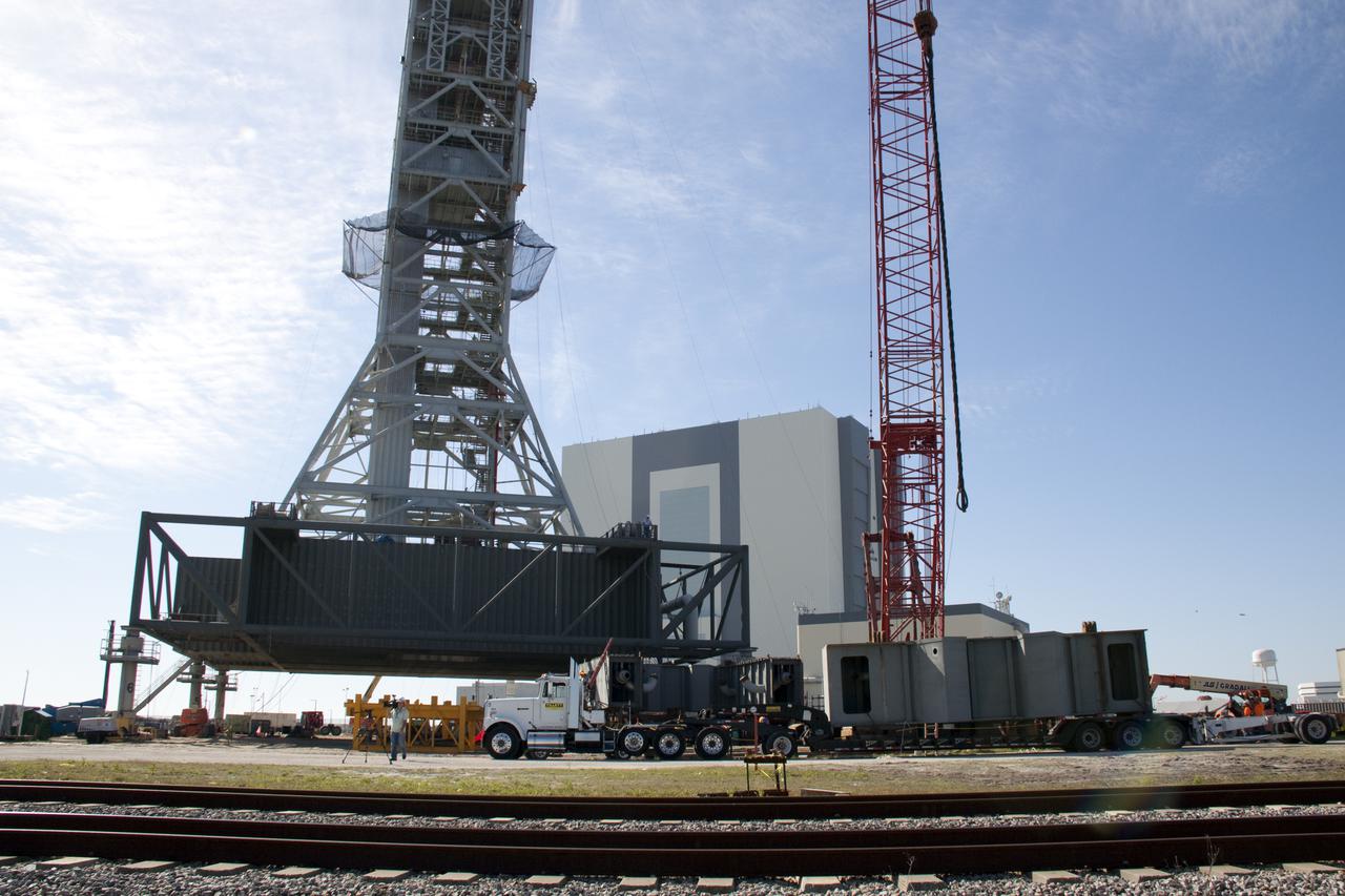 CAPE CANAVERAL, Fla. – At NASA's Kennedy Space Center in Florida, a tractor-trailer delivers the fourth segment of the launch mount for a new mobile launcher, or ML, being constructed to support NASA's future human spaceflight program.  The launcher's tower looms over the cab of the tractor.  In the background is the 525-foot-tall Vehicle Assembly Building.  The construction is taking place in the mobile launcher park site north of Kennedy's Vehicle Assembly Building.  The new launcher is 355 feet tall and has multiple platforms for personnel access. The base of the launcher is lighter than space shuttle mobile launcher platforms so the crawler-transporter can pick up the heavier load of the tower and a taller rocket. For information on NASA's future plans, visit http:__www.nasa.gov. Photo credit: NASA_Troy Cryder