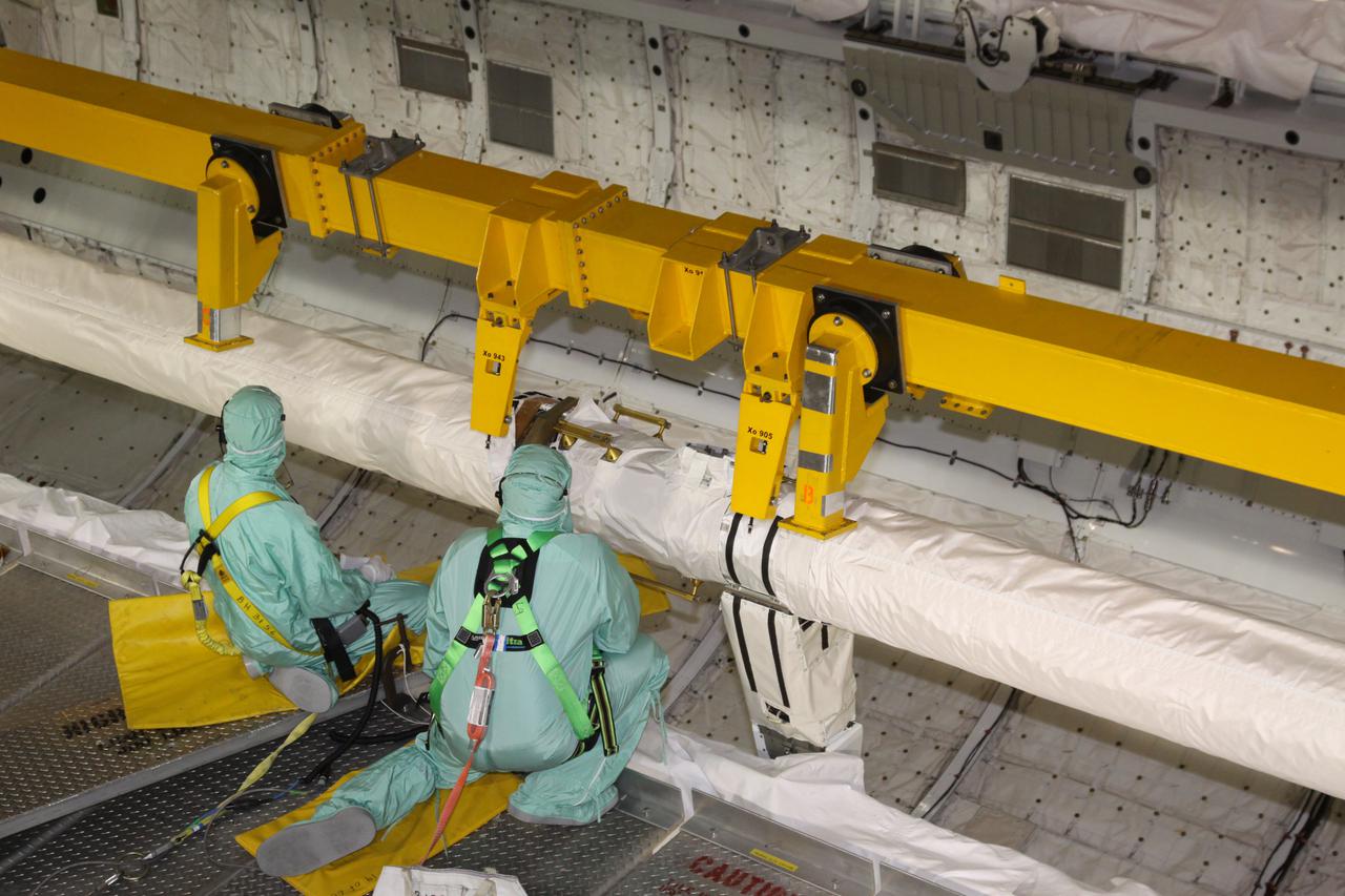CAPE CANAVERAL, Fla. - In Orbiter Processing Facility-3 at NASA's Kennedy Space Center in Florida, workers monitor a lifting device as it grapples the orbiter boom sensor system, or OBSS, in space shuttle Discovery's payload bay.  The workers are dressed in clean-room attire, known as 'bunny suits.' The 50-foot-long OBSS attaches to the end of the shuttle’s robotic arm and supports the cameras and laser systems used to inspect the shuttle’s thermal protection system while in space.  The OBSS' inspection boom assembly, or IBA, is removed from the arm every other processing flow for a detailed inspection. After five consecutive flights, all IBA internal components are submitted to a thorough electrical checkout in Kennedy's Remote Manipulator System Lab.  Discovery next will deliver the first Permanent Multi-purpose Module, or PMM; the Express Logistics Carrier 4; and critical spare parts to the International Space Station on the STS-133 mission.  Launch is targeted for Sept. 16.  Photo credit: NASA_Jack Pfaller
