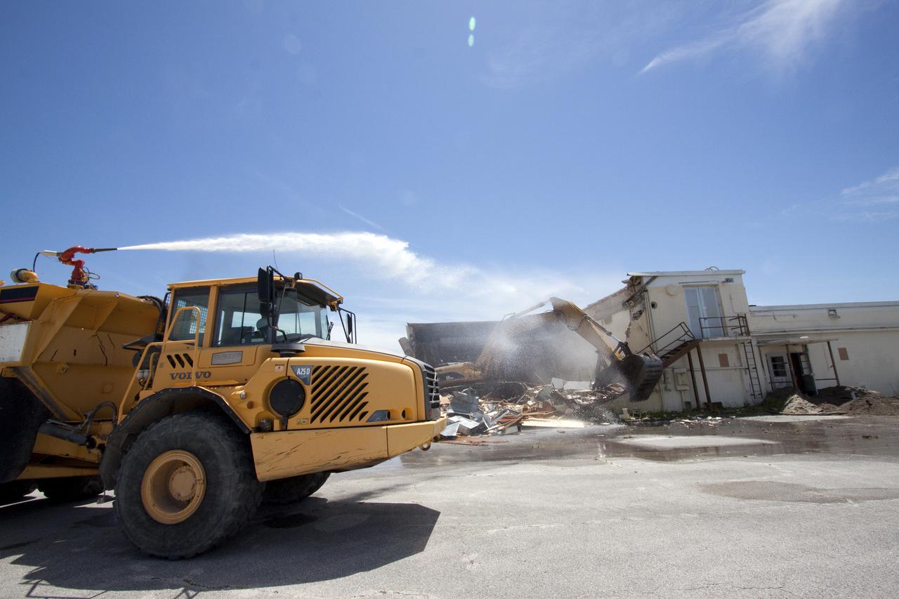 CAPE CANAVERAL, Fla. – At Cape Canaveral Air Force Station in Florida, a custom-built end dump truck spews water over the Mercury Mission Control Center to reduce the particles dispensed into the air by a Caterpillar 330 track-hoe tearing down the building.  The truck's operator controls the water spray using joy sticks installed in the cab of the truck.  The original building, constructed between 1956 and 1958, was last modified in 1963.  The center succumbed to the two worst enemies of structures along the space coast - time and salt air - necessitating that it be demolished as a safety measure.  The facility served as mission control during all the Project Mercury missions, as well as the first three flights of the Gemini Program. The center housed the flight controllers whose duty was to take over flight control after liftoff and follow it through until splashdown. Additionally, it supported vehicle checkout, spacecraft tracking, and astronaut training. With Gemini IV, mission control moved to Houston, and the facility took on the roles of launch control and tracking station. In 1999, much of the equipment and furnishings from the flight control area was moved to Kennedy Space Center's Visitor Complex.  A re-created mission control room currently is on display in the complex's Dr. Kurt H. Debus Conference Facility.  Speegle II of Cocoa, Fla., was awarded the contract for the deconstruction project.  Frank-Lin Excavating is performing the demolition for Sunrise Systems of Brevard, a subcontractor to Speegle II.  Photo credit: NASA_Jack Pfaller