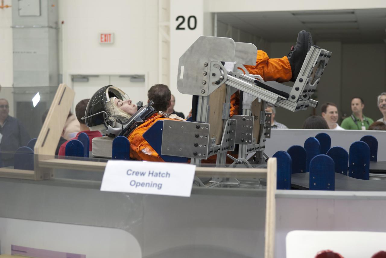 CAPE CANAVERAL, Fla. – In the Operations and Checkout Building at NASA's Kennedy Space Center in Florida, United Space Alliance EV_IV Integrated Operations work control specialist Jennifer Peterson, dressed in a flight-and-entry suit, demonstrates the placement of an astronaut inside a mock-up of an Orion crew exploration vehicle. The mock-up details the interior components of the vehicle including seat layout and the subsystem components on the outside of the pressure vessel. Orion mock-ups also have been used to verify accessibility of the servicing locations at the launch pad and in the Vehicle Assembly Building. For information on the development of the Orion capsule, visit www.nasa.gov_orion. Photo credit: NASA_Jim Grossmann