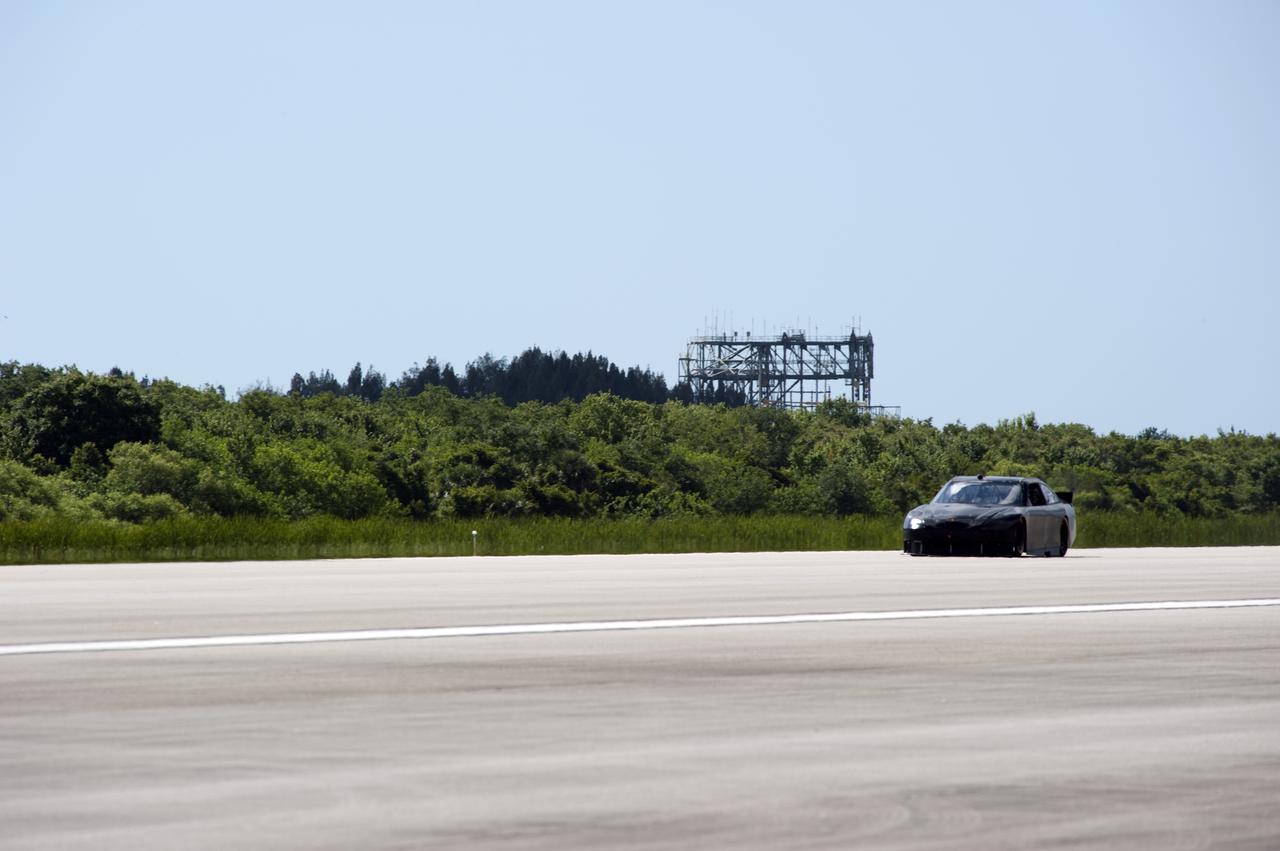CAPE CANAVERAL, Fla. – At NASA's Kennedy Space Center in Florida, NASCAR racer Matt DiBenedetto drives an instrument-laden Toyota down the three-mile-long Shuttle Landing Facility runway. The operation was part Joe Gibbs Racing's program to test aerodynamic and real-world capabilities on one of the flattest surfaces in the world. Behind the car is the space shuttle's Mate-Demate Device. Racing teams have been using the runway for testing since 2008. Joe Gibbs Racing signed a Space Act Agreement with NASA in May to use the facility's runway. Photo Credit: NASA_Kim Shiflett