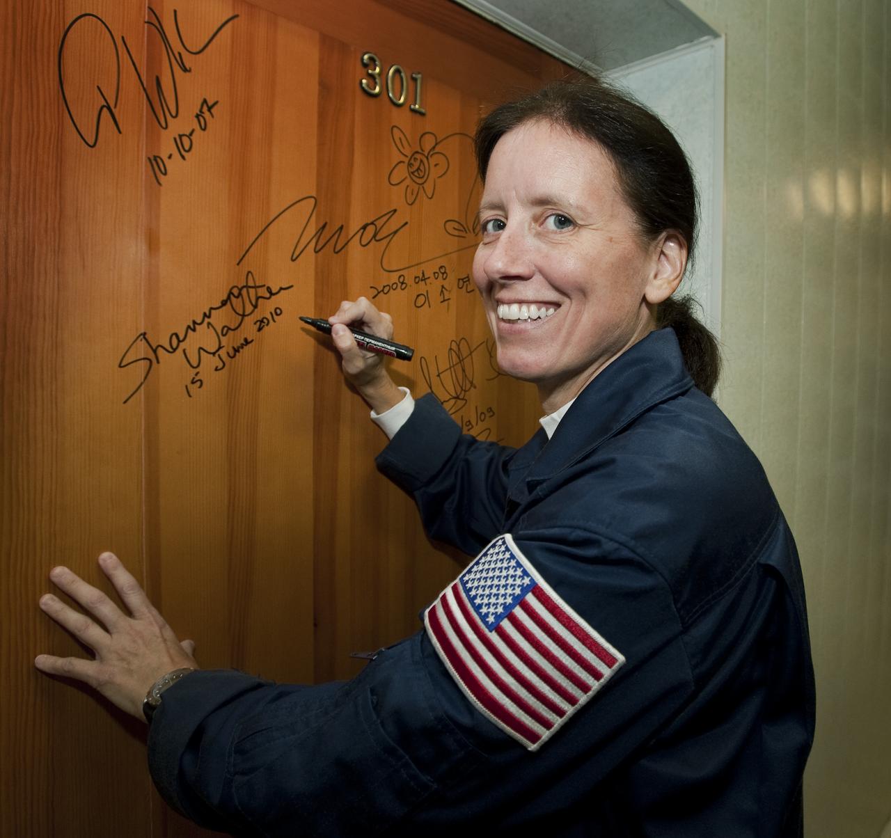 Expedition 24 NASA Flight Engineer Shannon Walker smiles for photographers after performing the traditional door signing at the Cosmonaut Hotel in Baikonur, Kazakhstan before departing with fellow crew members, Soyuz Commander Fyodor Yurchikhin of Russia, and NASA Flight Engineer Doug Wheelock to suit up for their launch, Tuesday, June 15, 2010.  Photo Credit: (NASA/Carla Cioffi)