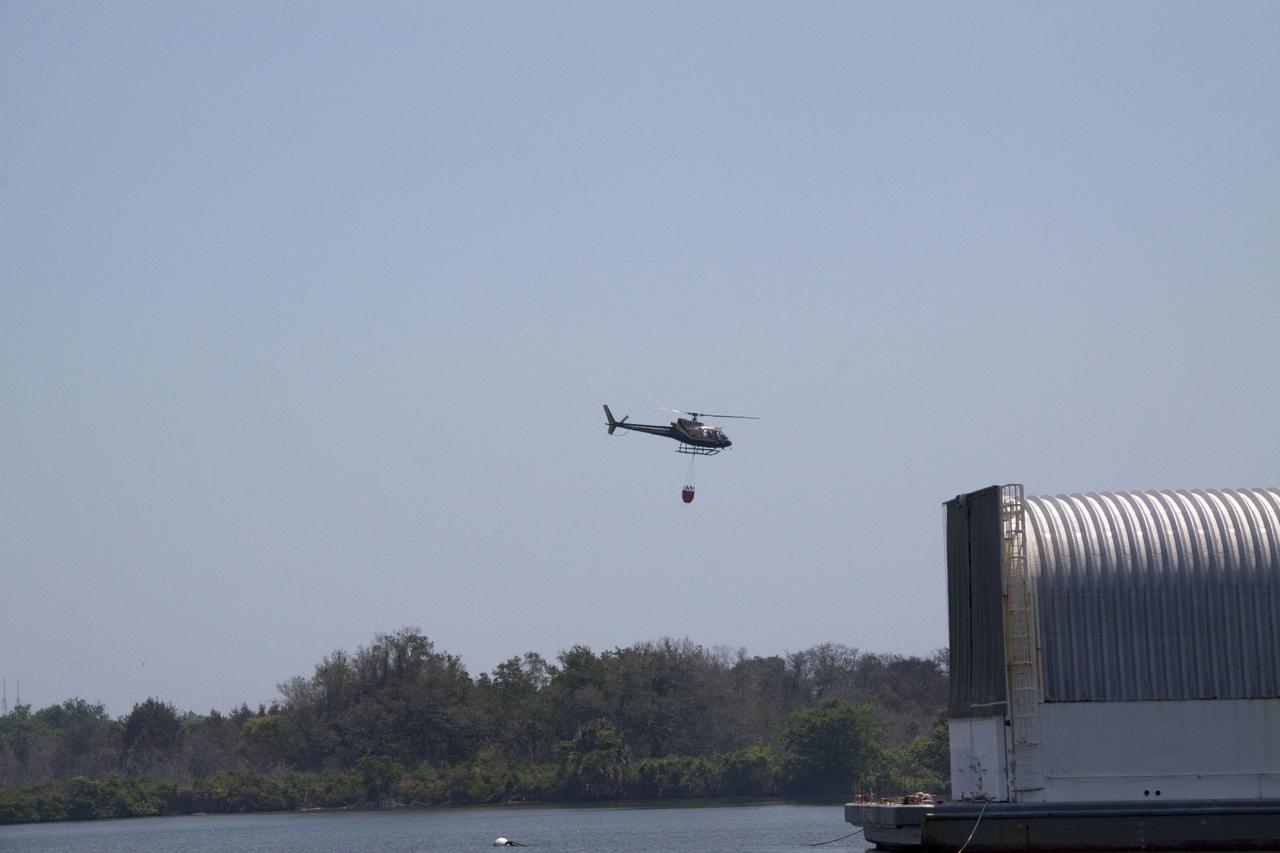 CAPE CANAVERAL, Fla. -- At NASA's Kennedy Space Center in Florida, a helicopter collects water from the Turn Basin to douse a nearby brush fire. The fire was spotted in a rural area southeast of Kennedy’s Press Site approximately three miles away from Launch Pad 39A, where space shuttle Endeavour awaits liftoff on the STS-134 mission to the International Space Station. The fire is being contained by crews from Kennedy and the U.S. Fish and Wildlife Service and smoke is not expected to impact launch. Photo credit: NASA_Jack Pfaller