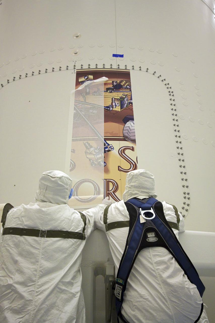 CAPE CANAVERAL, Fla. – In the Payload Hazardous Servicing Facility at NASA's Kennedy Space Center in Florida, two technicians carefully apply the Mars Science Laboratory (MSL) mission logo to the exterior of an Atlas V rocket's payload fairing. Tucked inside the fairing is the MSL spacecraft, including a compact car-sized rover, Curiosity, which has 10 science instruments designed to search for evidence on whether Mars has had environments favorable to microbial life, including the chemical ingredients for life. The unique rover will use a laser to look inside rocks and release its gasses so that the rover’s spectrometer can analyze and send the data back to Earth. Launch of MSL aboard a United Launch Alliance Atlas V rocket is planned for Nov. 25 from Space Launch Complex-41 on Cape Canaveral Air Force Station. For more information, visit http:__www.nasa.gov_msl. Photo credit: NASA_Jim Grossmann