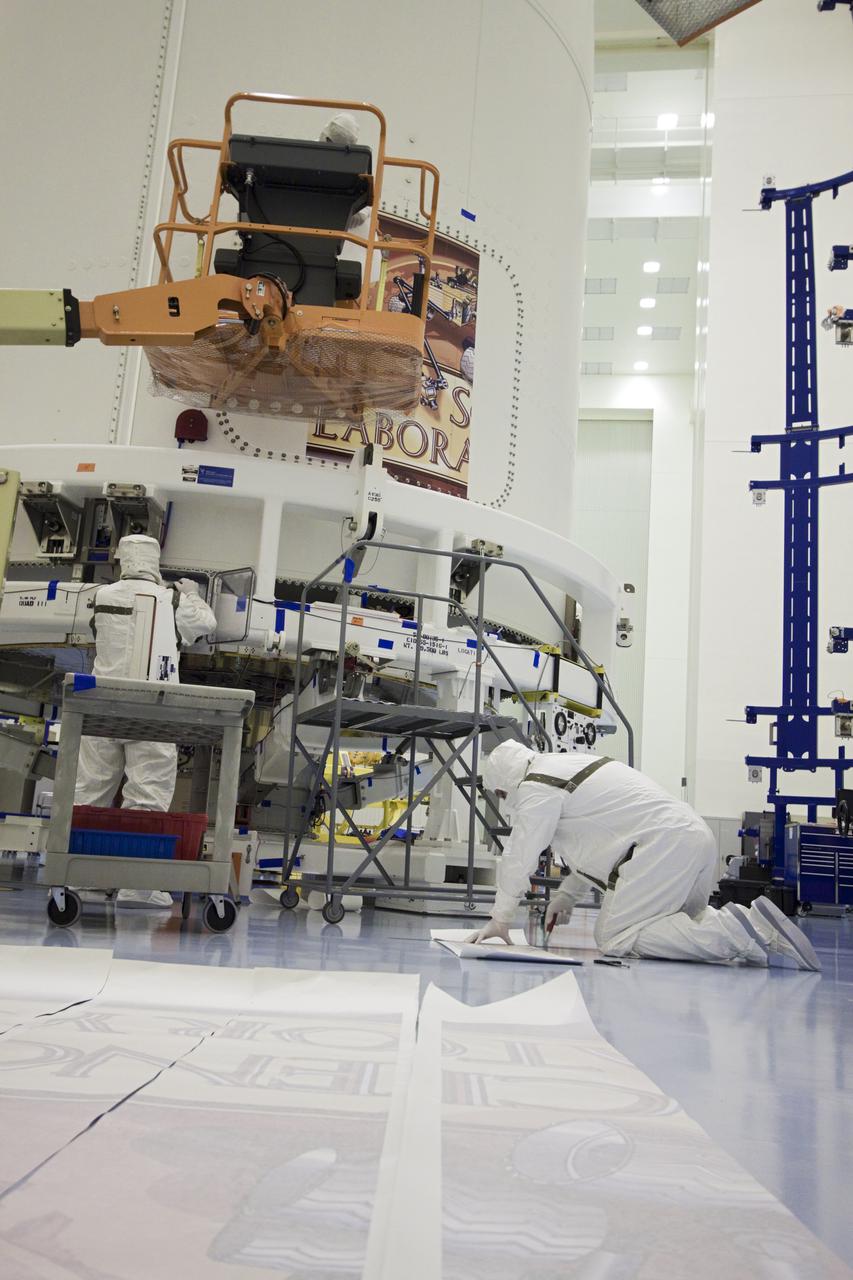 CAPE CANAVERAL, Fla. – Technicians inside NASA Kennedy Space Center's Payload Hazardous Servicing Facility use a lift to position a section of the Mars Science Laboratory (MSL) mission logo on the exterior of an Atlas V rocket's payload fairing. Tucked inside the fairing is the MSL spacecraft, including a compact car-sized rover, Curiosity, which has 10 science instruments designed to search for evidence on whether Mars has had environments favorable to microbial life, including the chemical ingredients for life.The unique rover will use a laser to look inside rocks and release its gasses so that the rover’s spectrometer can analyze and send the data back to Earth. Launch of MSL aboard a United Launch Alliance Atlas V rocket is planned for Nov. 25 from Space Launch Complex-41 on Cape Canaveral Air Force Station. For more information, visit http:__www.nasa.gov_msl. Photo credit: NASA_Jim Grossmann