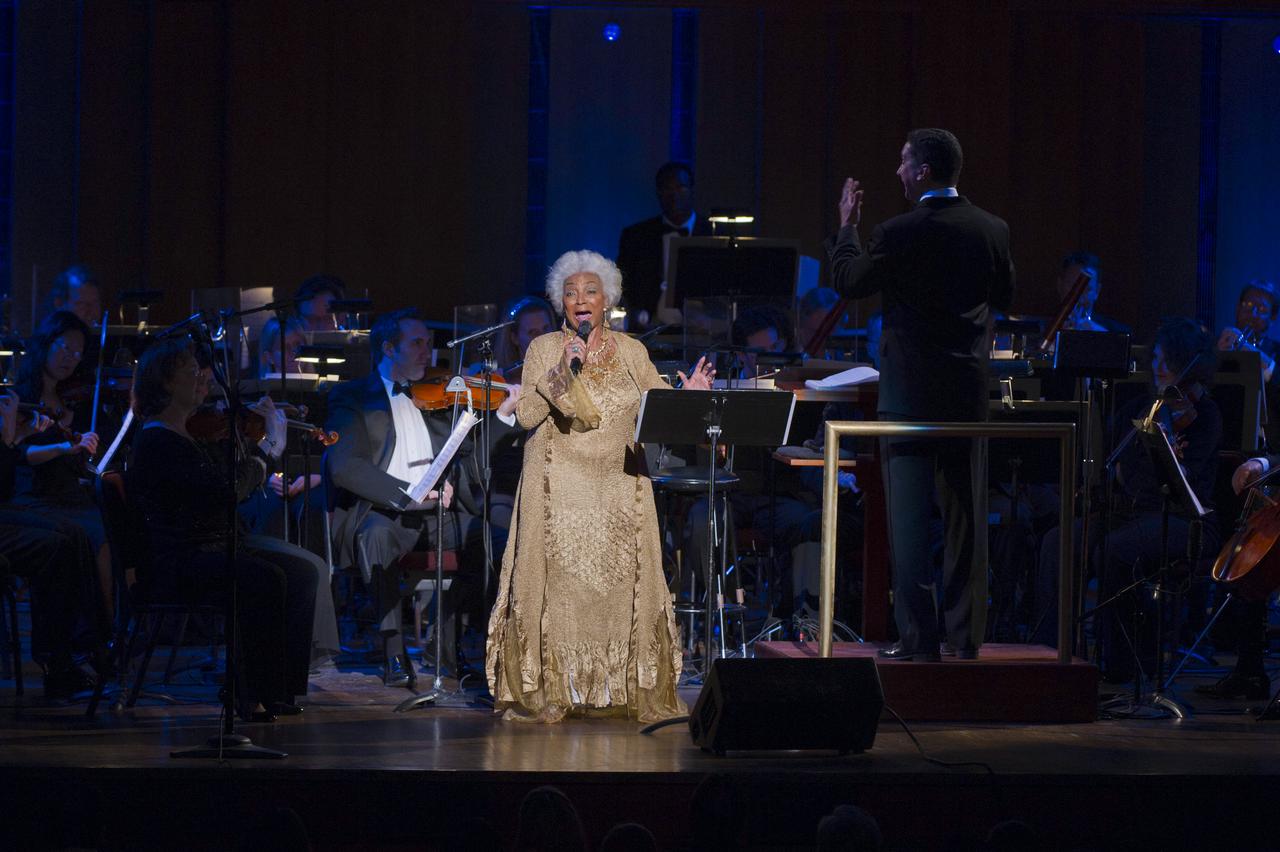 Actress Nichelle Nichols, best known for her role as communications officer Lieutenant Uhura in the series "Star Trek", sings as Emil de Cou, right, conducts the Space Philharmonic, Wednesday, May 25, 2011, in the concert hall at the John F. Kennedy Center for the Performing Arts in Washington. The event marked the 50th Anniversary of President John F. Kennedy's Special Message to the Congress on Urgent National Needs in which he stated "landing a man on the moon and returning him safely to earth". Photo Credit: (NASA/Paul E. Alers)