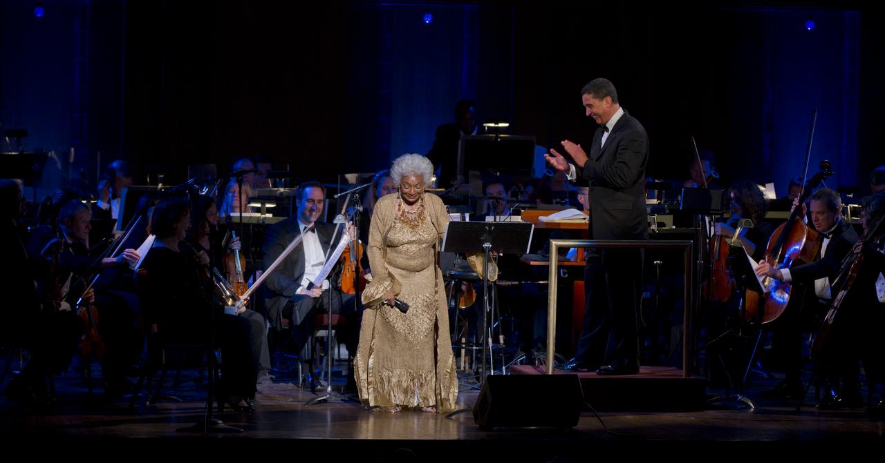 Actress Nichelle Nichols, best known for her role as communications officer Lieutenant Uhura in the series "Star Trek", bows as Emil de Cou, right, applauds, Wednesday, May 25, 2011, in the concert hall at the John F. Kennedy Center for the Performing Arts in Washington. The event marked the 50th Anniversary of President John F. Kennedy's Special Message to the Congress on Urgent National Needs in which he stated "landing a man on the moon and returning him safely to earth". Photo Credit: (NASA/Paul E. Alers)