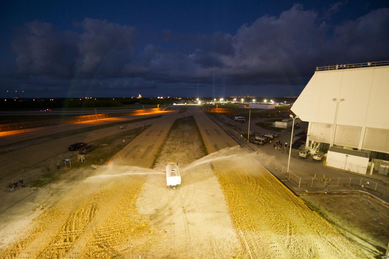 A truck sprays water on the crawler way to help minimize dust as the space shuttle Atlantis (STS-135), atop of the Mobile Launch Platform (MLP), rolls out of High Bay 3 in the Vehicle Assembly Building to Launch Pad 39a for its final flight, Tuesday evening, May 31, 2011, at Kennedy Space Center in Cape Canaveral, Fla. The 3.4-mile trek, known as "rollout," will take about seven hours to complete. Atlantis will carry the Raffaello multipurpose logistics module to deliver supplies, logistics and spare parts to the International Space Station. The launch of STS-135 is targeted for July 8. Photo Credit: (NASA/Bill Ingalls)