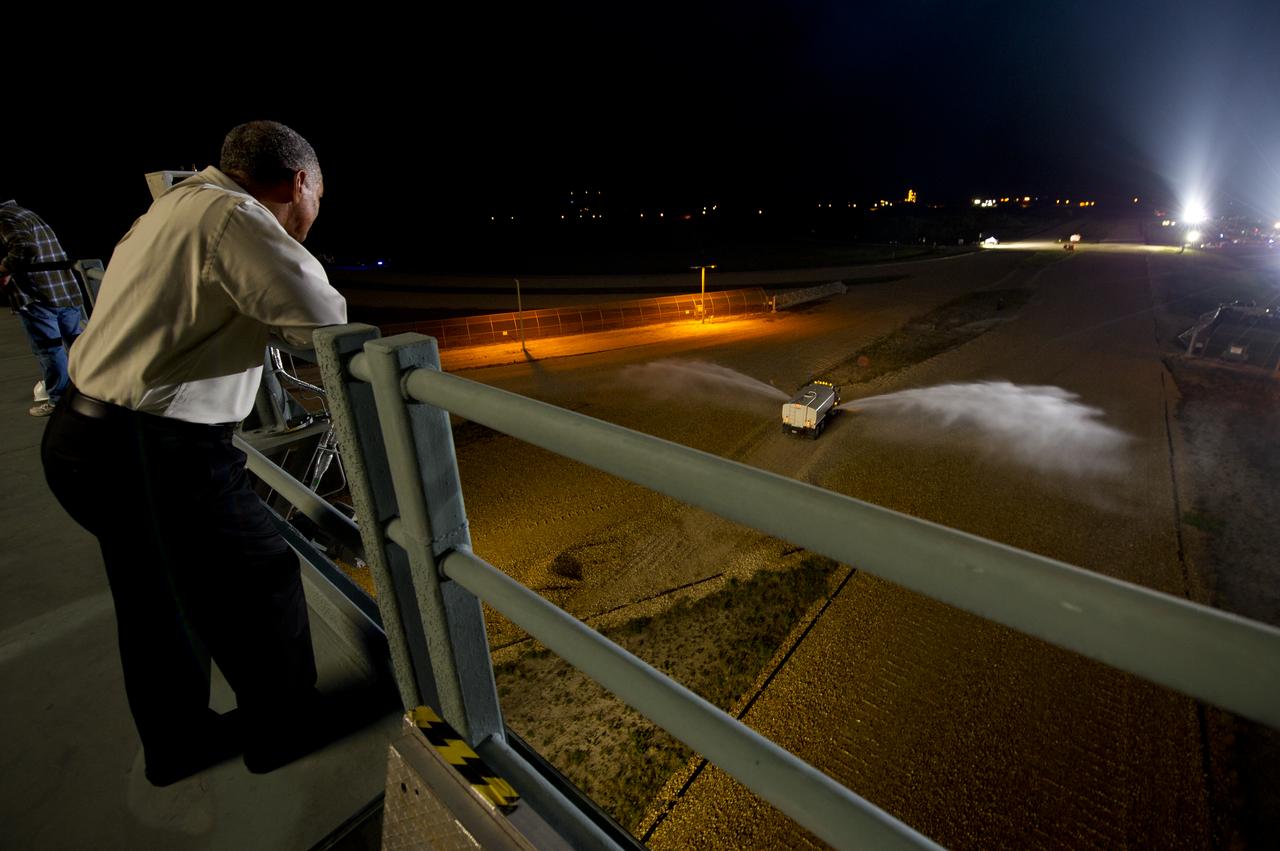 NASA Administrator Charles Bolden watches as a truck sprays water on the crawler way to help minimize dust as the space shuttle Atlantis (STS-135), atop of the Mobile Launch Platform (MLP), rolls out of High Bay 3 in the Vehicle Assembly Building to Launch Pad 39a for its final flight, Tuesday evening, May 31, 2011, at Kennedy Space Center in Cape Canaveral, Fla. The 3.4-mile trek, known as "rollout," will take about seven hours to complete. Atlantis will carry the Raffaello multipurpose logistics module to deliver supplies, logistics and spare parts to the International Space Station. The launch of STS-135 is targeted for July 8. Photo Credit: (NASA/Bill Ingalls)