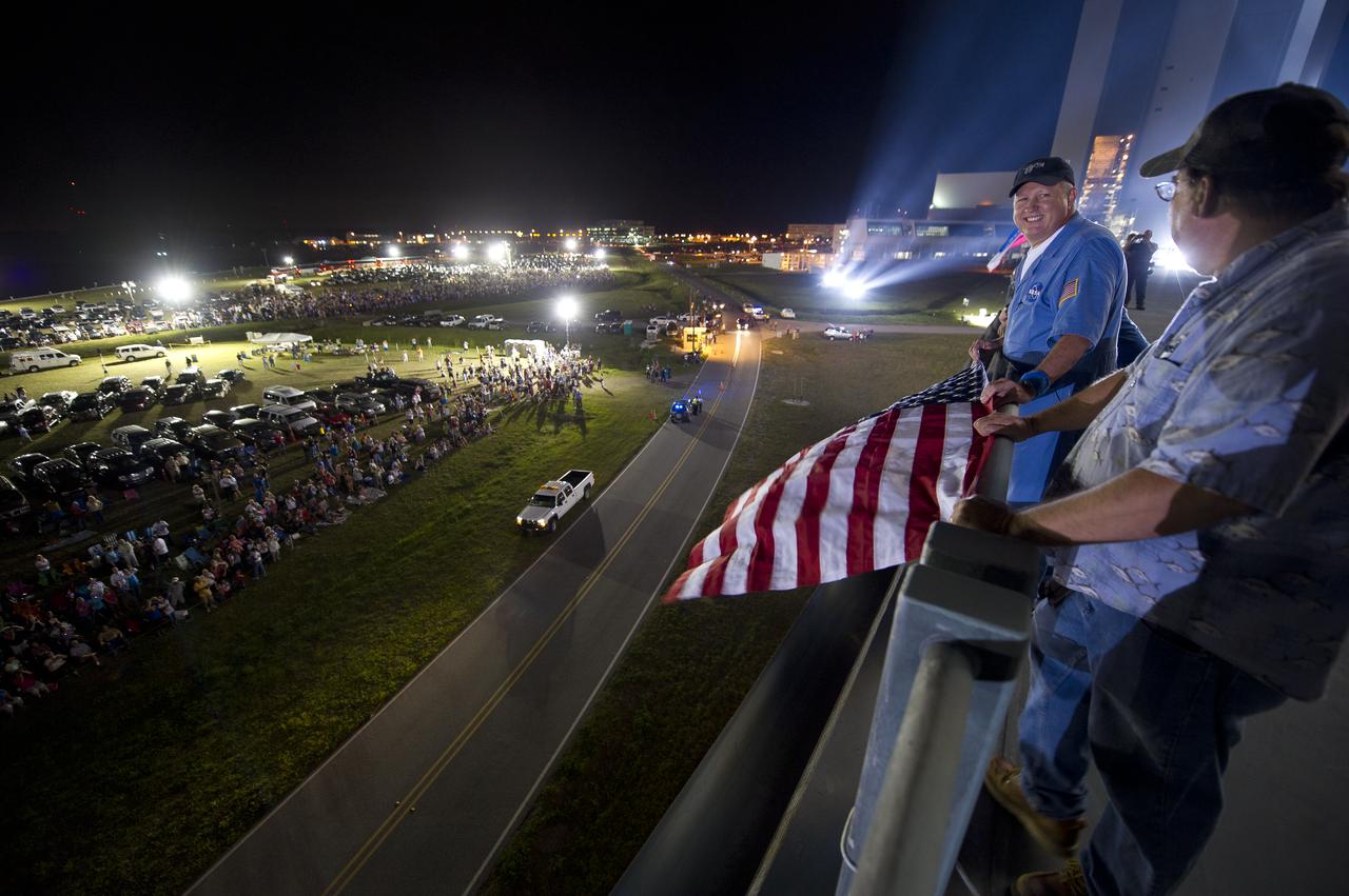 United Space Alliance Senior Space Shuttle Technician Mitchell Bromwell, left, and Randy Meyers of United Space Alliance display an American flag that has been flown all over the world by the U.S. military from atop the Mobile Launch Platform (MLP) as the space shuttle Atlantis begins its journey from High Bay 3 in the Vehicle Assembly Building to Launch Pad 39a for its final flight, Tuesday evening, May 31, 2011, at Kennedy Space Center in Cape Canaveral, Fla. The 3.4-mile trek, known as "rollout," will take about seven hours to complete. Atlantis will carry the Raffaello multipurpose logistics module to deliver supplies, logistics and spare parts to the International Space Station. The launch of STS-135 is targeted for July 8. Photo Credit: (NASA/Bill Ingalls)