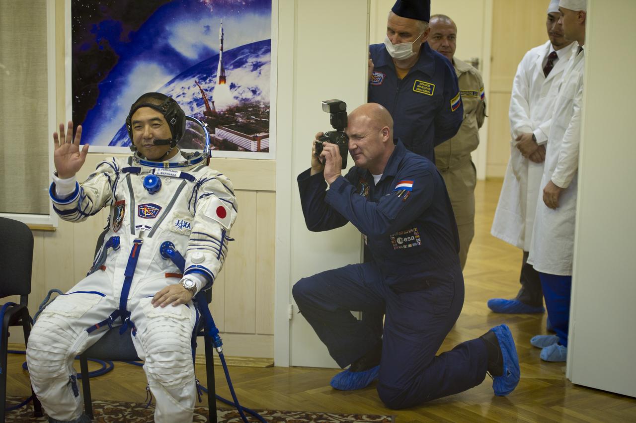 Expedition 28 Flight Engineer and JAXA (Japanese Aerospace Exploration Agency) astronaut Satoshi Furukawa, left, waves to friends and family while he waits to have his Russian Sokol suit pressure checked on Tuesday, June 7, 2011 at the Baikonur Cosmodrome in Kazakhstan.  Expedition 28 backup Flight Engineer and ESA (European Space Agency) astronaut Andre Kuipers is behind the camera taking photographs.  Photo Credit:  (NASA/Carla Cioffi)