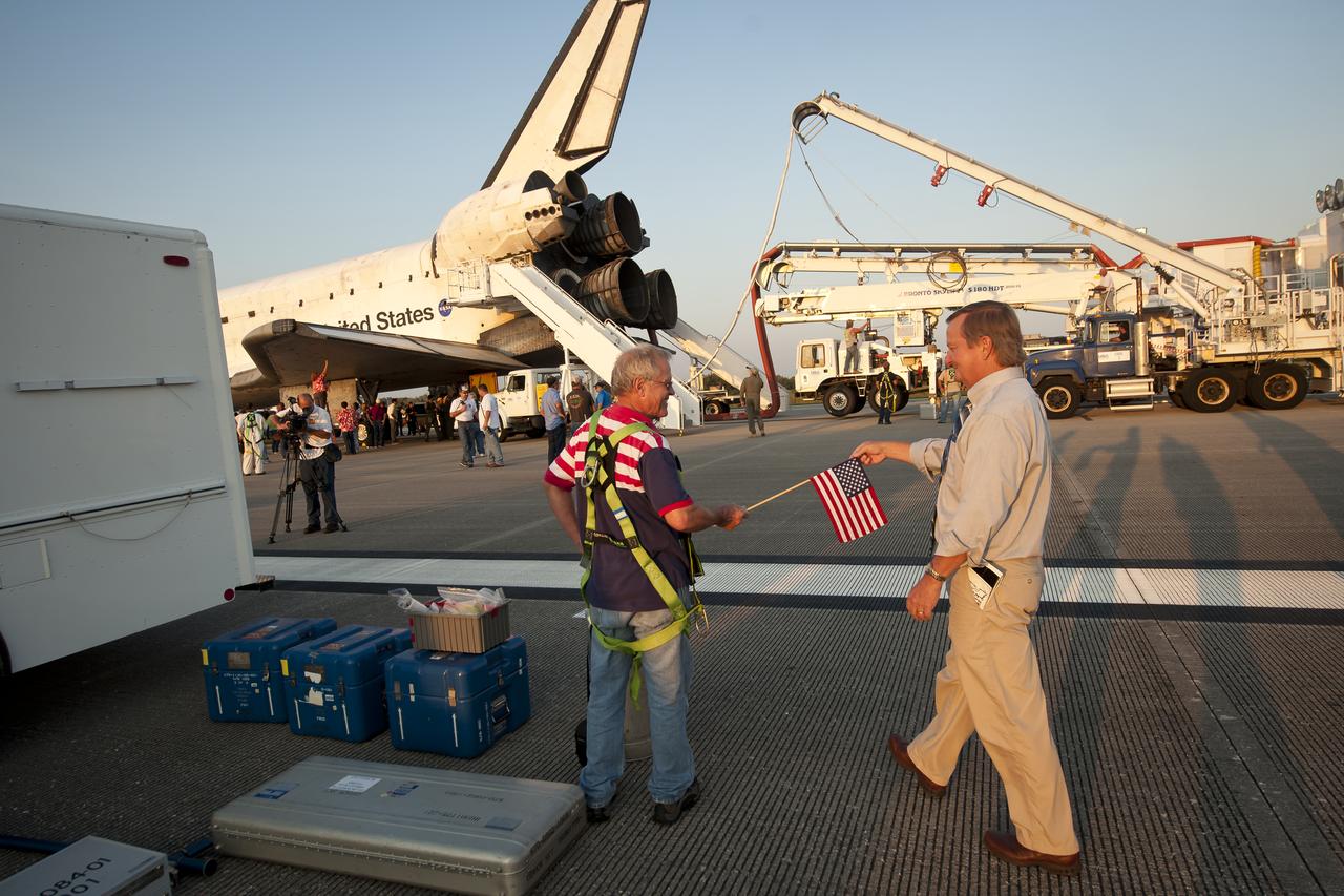 NASA Launch Director Michael Leinbach, right, hands an American flag to a worker on the runway of the Shuttle Landing Facility (SLF) shortly after the space shuttle Atlantis (STS-135) landed early Thursday morning, July 21, 2011, in Cape Canaveral, Fla. Overall, Atlantis spent 307 days in space and traveled nearly 126 million miles during its 33 flights. Atlantis, the fourth orbiter built, launched on its first mission on Oct. 3, 1985. Photo Credit: (NASA/Bill Ingalls)
