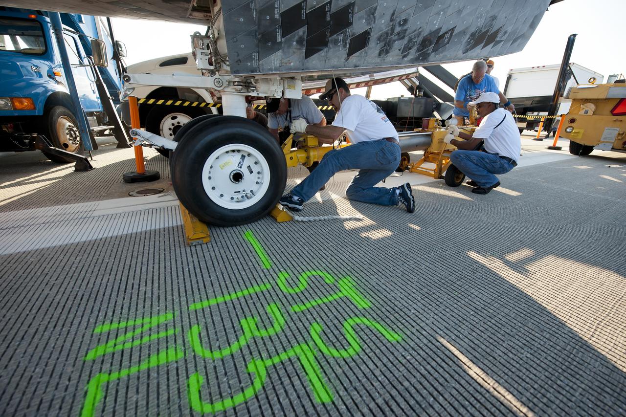 NASA and contractor personnel work to secure the tow bar onto the space shuttle Atlantis at the Kennedy Space Center Shuttle Landing Facility (SLF) shortly after Atlantis (STS-135) landed early Thursday morning, July 21, 2011, in Cape Canaveral, Fla. The runway is marked to show where the nose landing gear wheels stopped. Overall, Atlantis spent 307 days in space and traveled nearly 126 million miles during its 33 flights. Atlantis, the fourth orbiter built, launched on its first mission on Oct. 3, 1985. Photo Credit: (NASA/Bill Ingalls)