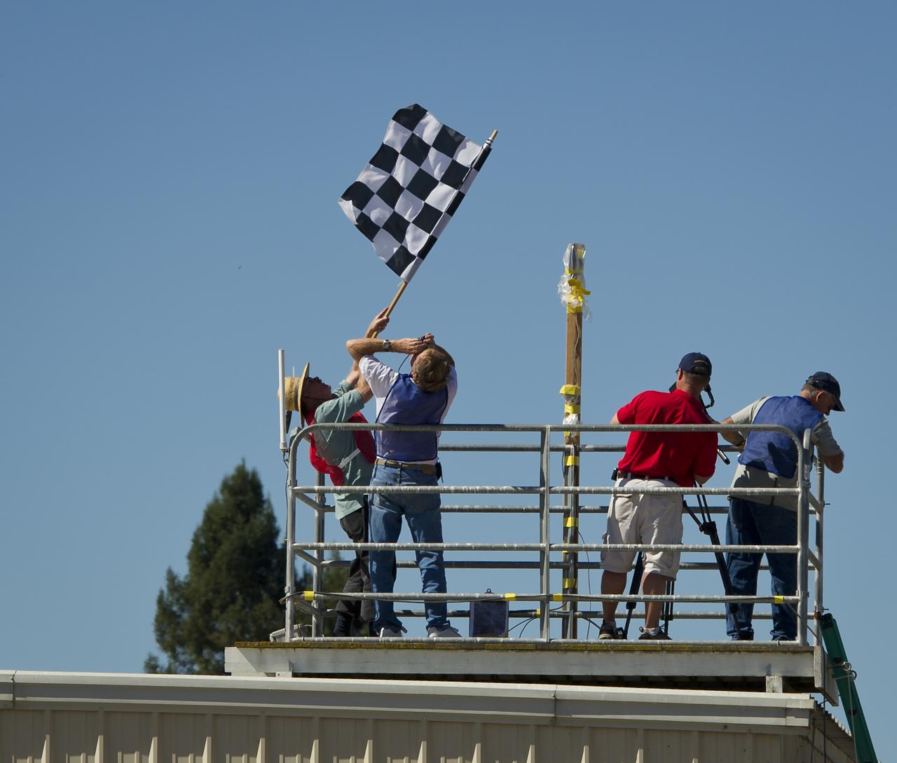 CAFE Foundation Hanger Boss Mike Fenn waves the checkered flag as aircraft pass the finish line of the miles per gallon (MPG) flight during the 2011 Green Flight Challenge, sponsored by Google, at the Charles M. Schulz Sonoma County Airport in Santa Rosa, Calif. on Tuesday, Sept. 27, 2011.  NASA and the Comparative Aircraft Flight Efficiency (CAFE) Foundation are having the challenge with the goal to advance technologies in fuel efficiency and reduced emissions with cleaner renewable fuels and electric aircraft. Photo Credit: (NASA/Bill Ingalls)