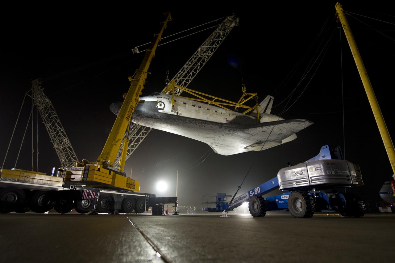 The space shuttle Discovery is suspended from a sling held by two cranes shortly after the NASA 747 Shuttle Carrier Aircraft (SCA) was pushed back from underneath at Washington Dulles International Airport, Thursday, April 19, 2012, in Sterling, VA.  Discovery, the first orbiter retired from NASA’s shuttle fleet, completed 39 missions, spent 365 days in space, orbited the Earth 5,830 times, and traveled 148,221,675 miles. NASA will transfer Discovery to the National Air and Space Museum to begin its new mission to commemorate past achievements in space and to educate and inspire future generations of explorers. Photo Credit: (NASA/Bill Ingalls)
