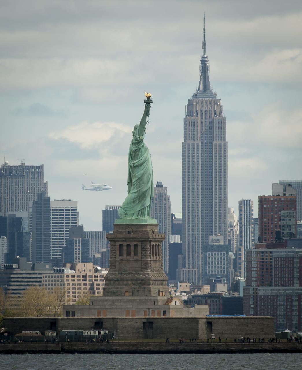 Space shuttle Enterprise, mounted atop a NASA 747 Shuttle Carrier Aircraft (SCA), is seen off in the distance behind the Statue of Liberty, Friday, April 27, 2012, in New York. Enterprise was the first shuttle orbiter built for NASA performing test flights in the atmosphere and was incapable of spaceflight. Originally housed at the Smithsonian's Steven F. Udvar-Hazy Center, Enterprise will be demated from the SCA and placed on a barge that will eventually be moved by tugboat up the Hudson River to the Intrepid Sea, Air & Space Museum in June. Photo Credit: (NASA/Bill Ingalls)