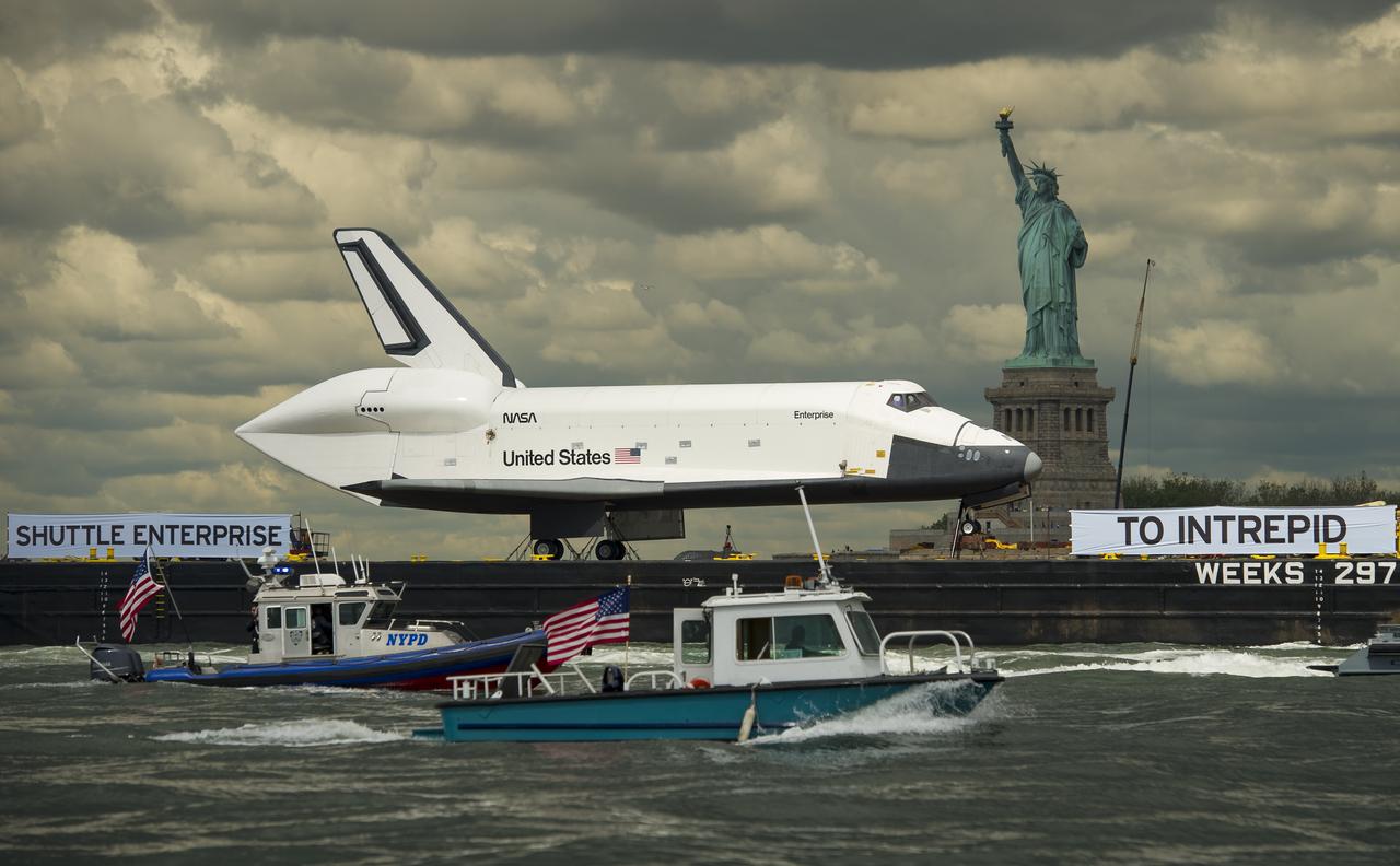 The space shuttle Enterprise, atop a barge,  passes the Statue of Liberty in New York on its way to the Intrepid Sea, Air and Space Museum where it will be permanently displayed, Wednesday, June 6, 2012. Photo Credit: (NASA/Bill Ingalls)