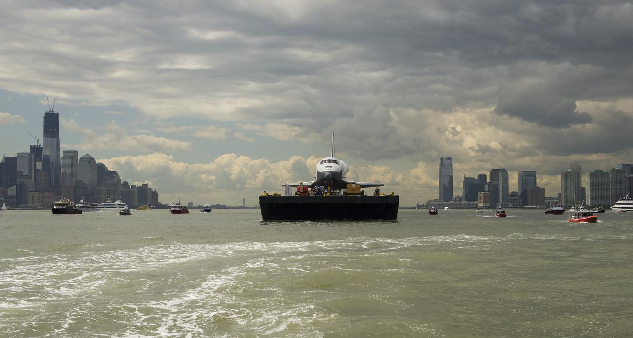 The space shuttle Enterprise is towed by barge up the Hudson River with the New York skyline seen on the left and the Jersey City skyline on the right while on it's way to the Intrepid Sea, Air and Space Museum where it will be permanently displayed, Wednesday, June 6, 2012. Photo Credit: (NASA/Bill Ingalls)