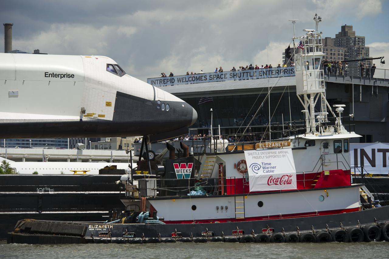The space shuttle Enterprise is towed by barge next to the Intrepid Sea, Air and Space Museum where it will lifted onto the flight deck to be placed on permanent display, Wednesday, June 6, 2012 in New York. Photo Credit: (NASA/Bill Ingalls)