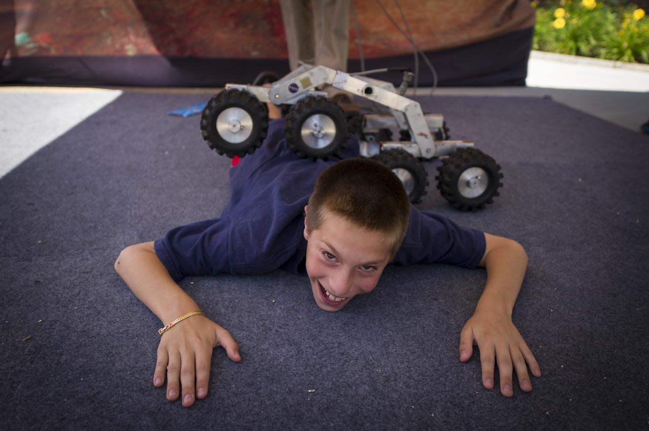 A visitor to the Worcester Polytechnic Institute (WPI) "TouchTomorrow" education and outreach event helps demonstrate how a NASA rover design enables the rover to climb over obstacles higher than it's own body on Saturday, June 16, 2012 at WPI in Worcester, Mass. The event was held in tandem with the NASA-WPI Sample Return Robot Centennial Challenge.  The NASA-WPI challenge tasked robotic teams to build autonomous robots that can identify, collect and return samples.  NASA needs autonomous robotic capability for future planetary exploration. Photo Credit: (NASA/Bill Ingalls)