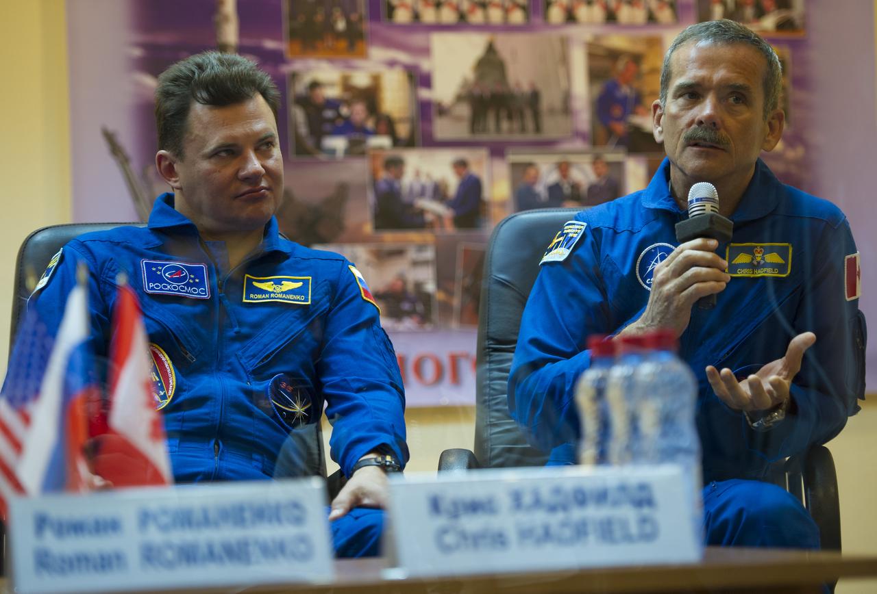 Quarantined Expedition 32 Canadian backup crewmember Chris Hadfield, right, answers reporters questions from behind glass during a prelaunch press conference held at the Cosmonaut Hotel on Friday, July 13, 2012 in Baikonur, Kazakhstan.  Seated next to him is Expedition 32 Russian backup crewmember Roman Romanenko.  Photo Credit (NASA/Carla Cioffi)