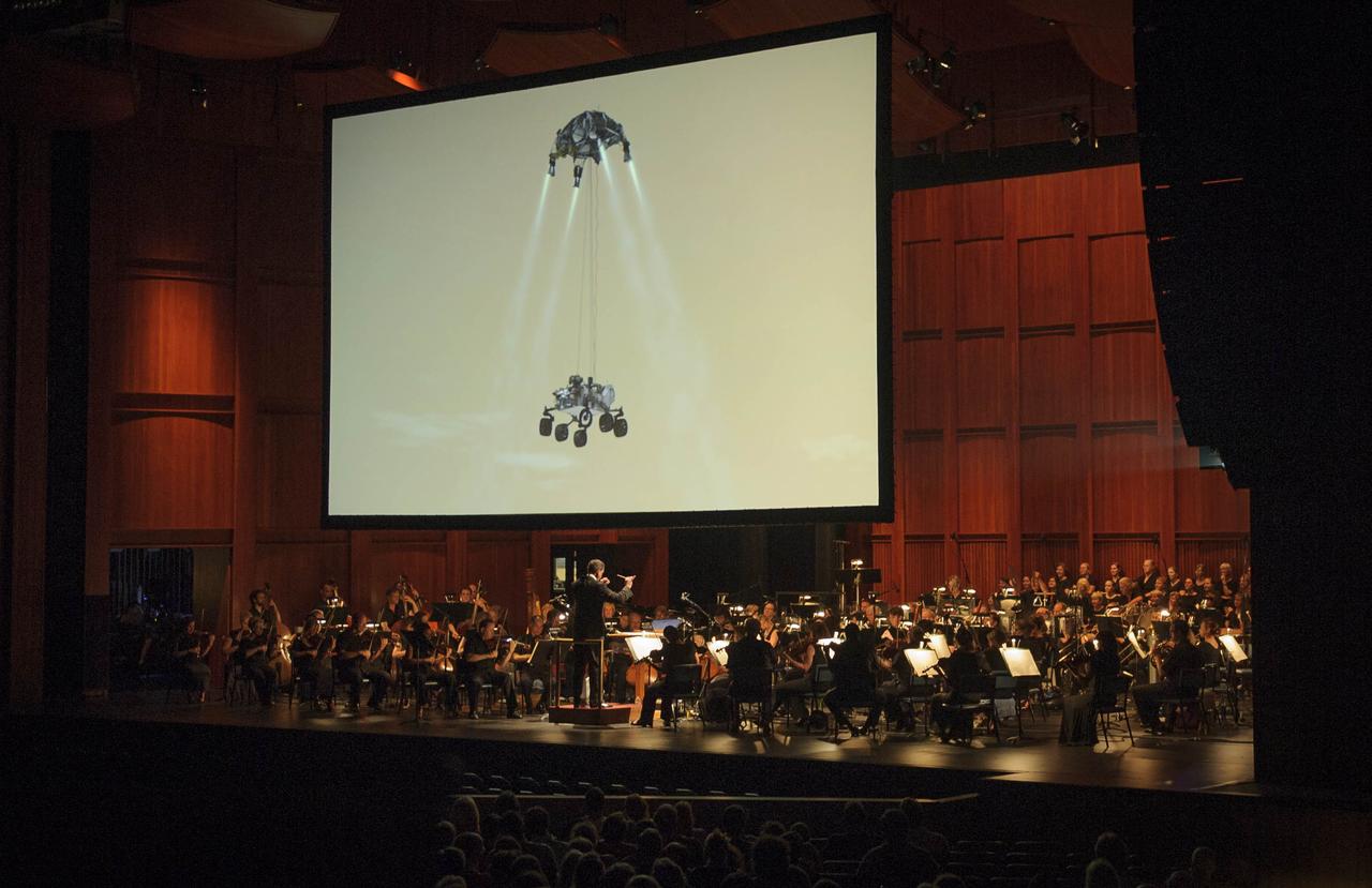 An image of the Mars rover Curiosity is seen on a giant screen as Emil de Cou, conducts the National Symphony Orchestra during a performance entitled "The Planets--An HD Odyessy", Friday evening, July 27, 2012, at the Wolf Trap National Park for the Performing Arts in Vienna, Va. Photo Credit: (NASA/Paul E. Alers)