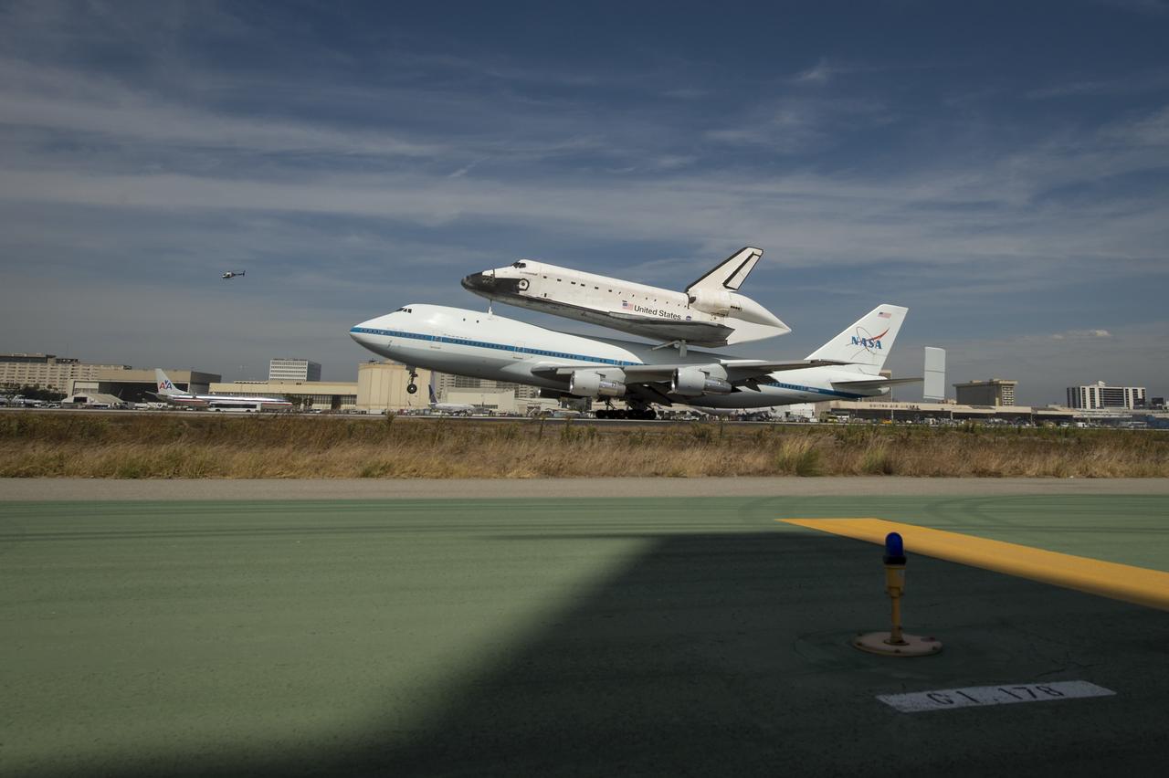 Space shuttle Endeavour, mounted atop a NASA 747 Shuttle Carrier Aircraft (SCA) lands at Los Angeles International Airport, Friday, Sept. 21, 2012. The shadow of a NASA F-18 chase jet wing is shown in the foreground.  Endeavour, built as a replacement for space shuttle Challenger, completed 25 missions, spent 299 days in orbit, and orbited Earth 4,671 times while traveling 122,883,151 miles. Beginning Oct. 30, the shuttle will be on display in the California Science center's Samuel Oschin Space Shuttle Endeavour  Display Pavilion, embarking on its new mission to commemorate past achievements in space and educate and inspire future generations of explorers.Photo Credit: (NASA/Bill Ingalls)