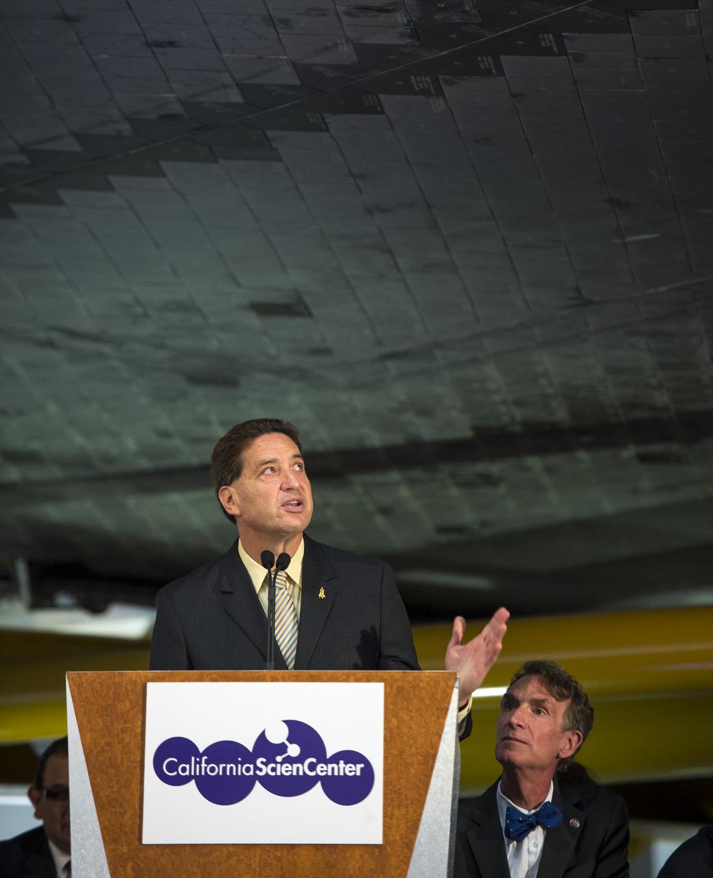 President and CEO of the California Science Center Jeffrey N. Rudolph speaks from a podium underneath the space shuttle Endeavour during the grand opening ceremony for the center's Samuel Oschin Space Shuttle Endeavour Display Pavilion, Tuesday, Oct. 30, 2012, in Los Angeles.  Endeavour, built as a replacement for space shuttle Challenger, completed 25 missions, spent 299 days in orbit, and orbited Earth 4,671 times while traveling 122,883,151 miles. Photo Credit: (NASA/Bill Ingalls)