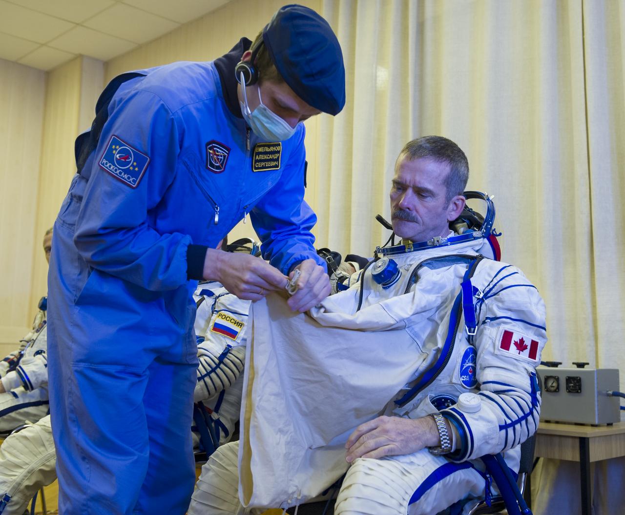 Expedition 34/35 Flight Engineer Chris Hadfield of CSA is helped into his Russian Sokol suit as he and fellow cremates, Soyuz Commander Roman Romanenko and Flight Engineer Tom Marshburn prepare for their Soyuz launch to the International Space Station, on Wednesday, Dec. 19, 2012, in Baikonur, Kazakhstan. Launch of the Soyuz rocket will send Hadfield, Romanenko and Marshburn on a five-month mission aboard the International Space Station.  Photo Credit: (NASA/GCTC/Andrey Shelepin)