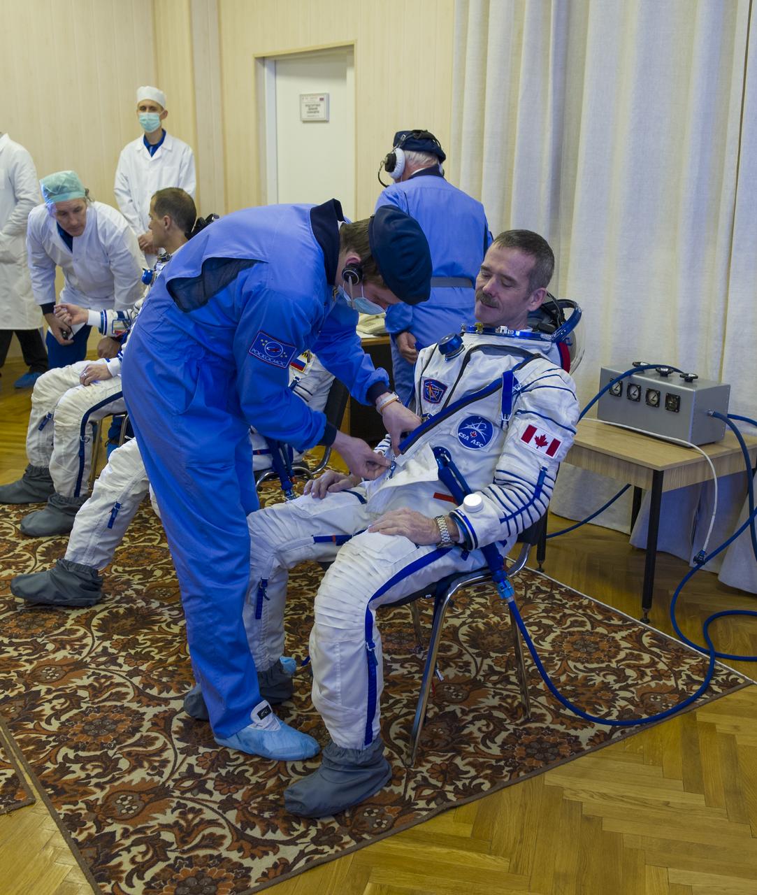 Expedition 34/35 Flight Engineer Chris Hadfield of CSA is helped into his Russian Sokol suit as he and fellow cremates, Soyuz Commander Roman Romanenko and Flight Engineer Tom Marshburn prepare for their Soyuz launch to the International Space Station, on Wednesday, Dec. 19, 2012, in Baikonur, Kazakhstan. Launch of the Soyuz rocket will send Hadfield, Romanenko and Marshburn on a five-month mission aboard the International Space Station.  Photo Credit: (NASA/GCTC/Andrey Shelepin)