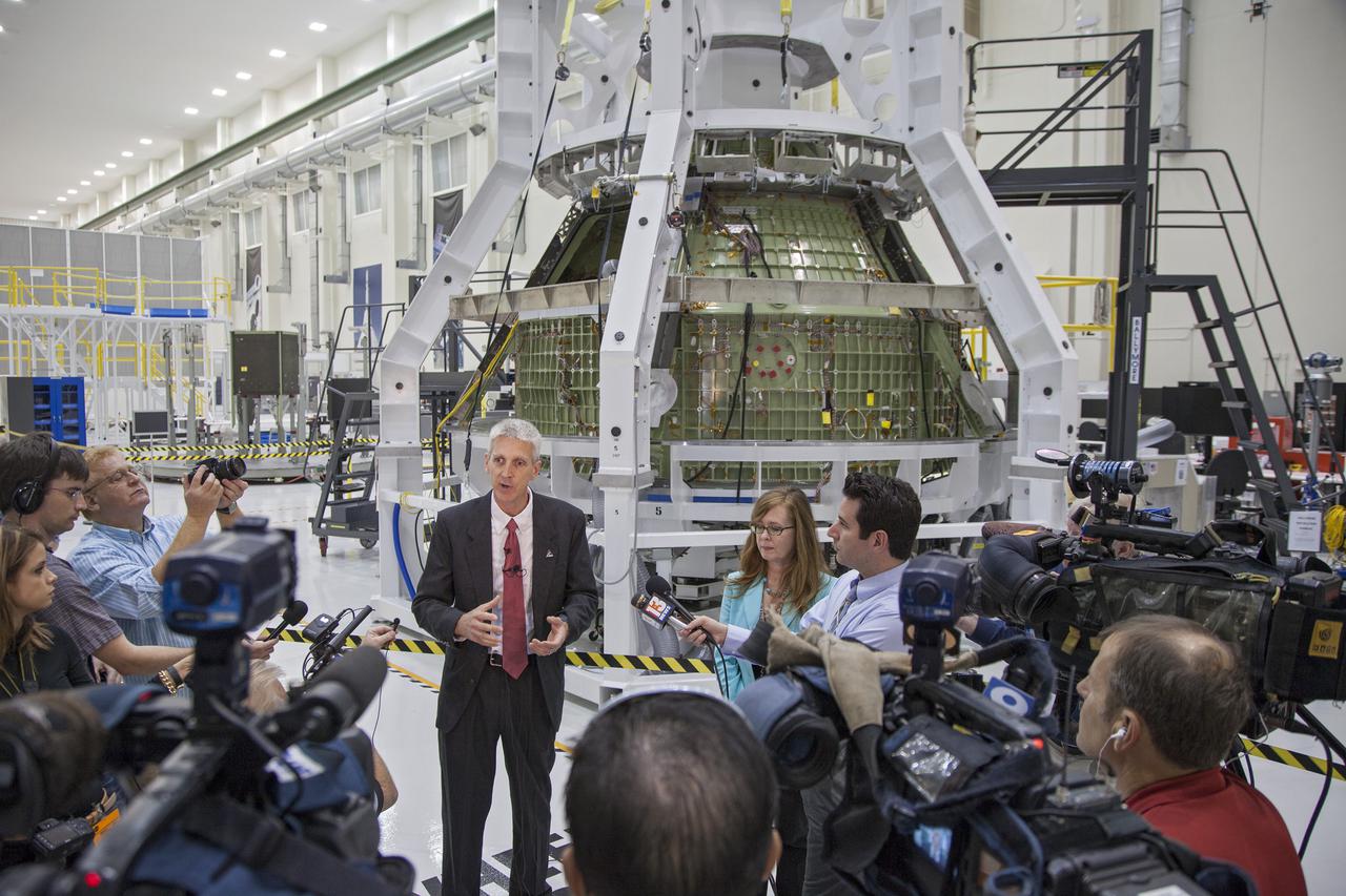 CAPE CANAVERAL, Fla. – Inside the high bay of Kennedy Space Center's Operations and Checkout Building, Scott Wilson, NASA's Orion production manager at the Florida Spaceport, briefs members of the news media about progress in preparing Orion for its first flight. In the background, the Orion spacecraft is surrounded by a special pre-launch processing access fixture.   Orion is the exploration spacecraft designed to carry crews to space beyond low Earth orbit. It will provide emergency abort capability, sustain the crew during the space travel and provide safe re-entry from deep space return velocities. The first unpiloted test flight of the Orion is scheduled to launch in 2014 atop a Delta IV rocket and in 2017 on a Space Launch System rocket. For more information, visit http:__www.nasa.gov_orion Photo credit: NASA_Kim Shiflett