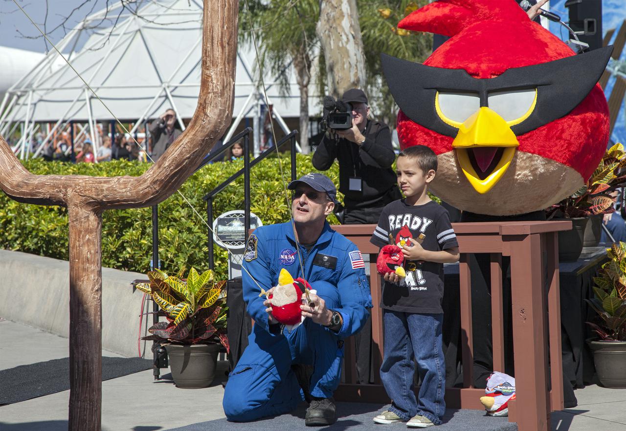CAPE CANAVERAL, Fla. -- At NASA’s Kennedy Space Center Visitor Complex in Florida, NASA astronaut Don Pettit uses a giant slingshot to launch a plush Angry Bird character during the grand opening of the new Angry Birds Space Encounter. Standing behind Pettit is Red Bird, one of the Angry Bird characters.  Finland-based Rovio Entertainment, the creator of the Angry Birds Space game, partnered with Kennedy Space Center to bring the beloved characters to life. It is the first Angry Birds interactive exhibit in the United States designed for people of all ages. The 4,485-square-foot facility hosts the space adventures of the Angry Birds as they travel into an intergalactic wormhole, come face-to-face with Space Pigs and discover heroic superpowers. Six interactive stations are designed to encourage children in science, technology, engineering and mathematics fields of study. Photo credit: NASA_Kim Shiflett