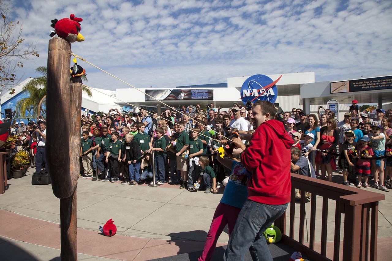 CAPE CANAVERAL, Fla. -- At NASA’s Kennedy Space Center Visitor Complex in Florida, Dan Mitchell, director of location-based entertainment for Rovio Entertainment, helps a child use a giant slingshot to launch a plush Angry Bird character during the grand opening of the new Angry Birds Space Encounter.   Finland-based Rovio Entertainment, the creator of the Angry Birds Space game, partnered with Kennedy Space Center to bring the beloved characters to life. It is the first Angry Birds interactive exhibit in the United States designed for people of all ages. The 4,485-square-foot facility hosts the space adventures of the Angry Birds as they travel into an intergalactic wormhole, come face-to-face with Space Pigs and discover heroic superpowers. Six interactive stations are designed to encourage children in science, technology, engineering and mathematics fields of study. Photo credit: NASA_Kim Shiflett