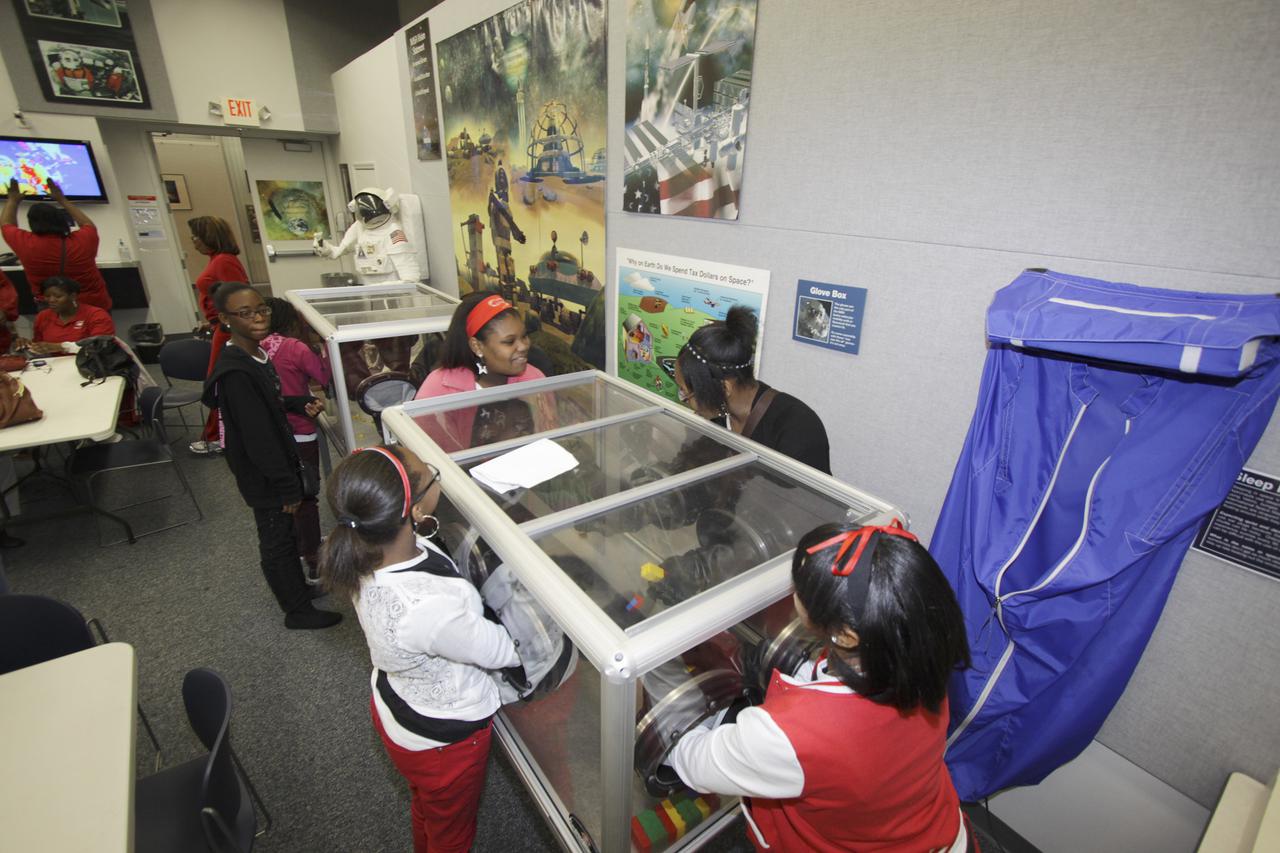 CAPE CANAVERAL, Fla. – Middle and High school students from Florida's Putnam and Volusia counties use a glove box practice working with materials with protected hands during a science demonstration at the NASA's Center for Space at the Kennedy Space Center.   The 11 to 18-year-old students are part of Delta Academy and Delta GEMS, an African American women’s mentoring program affiliated with Delta Sigma Theta. The sorority uses their collective efforts to promote academic excellence, provide scholarships and support underserved students. As a part of the science program, the young scholars participated in a presentation by professional women who work at Kennedy discussing career choices and encouraging interest in science, technology, engineering and mathematics STEM careers. Photo credit: NASA_Jim Grossmann