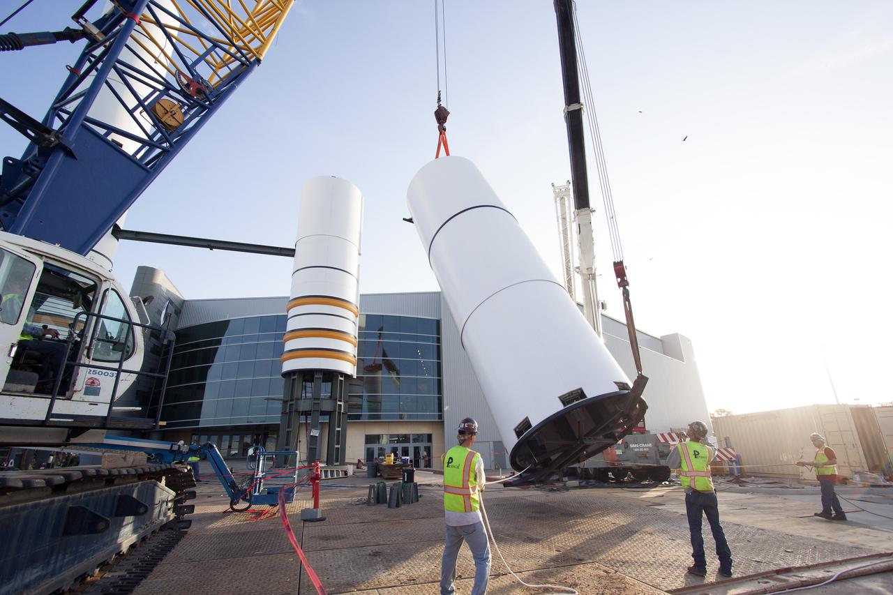CAPE CANAVERAL, Fla. – A crane lifts a segment for a set of twin, full-size replica Solid Rocket Boosters SRBs in front of the Space Shuttle Atlantis exhibit under construction at the Kennedy Space Center Visitor Complex in Florida. Atlantis is housed in the building behind the SRB stack. An external tank replica will be added later to the middle of the SRBs to complete the display. The SRBs stand 150 feet tall, while the external tank will reach 184 feet when it is finished. The shuttle was mounted to the stack and depended on the power of the SRBs to lift it off the launch pad and start it on its way to space. The external tank was loaded with liquid propellants for the shuttle's three main engines. Photo credit: NASA_Jim Grossmann