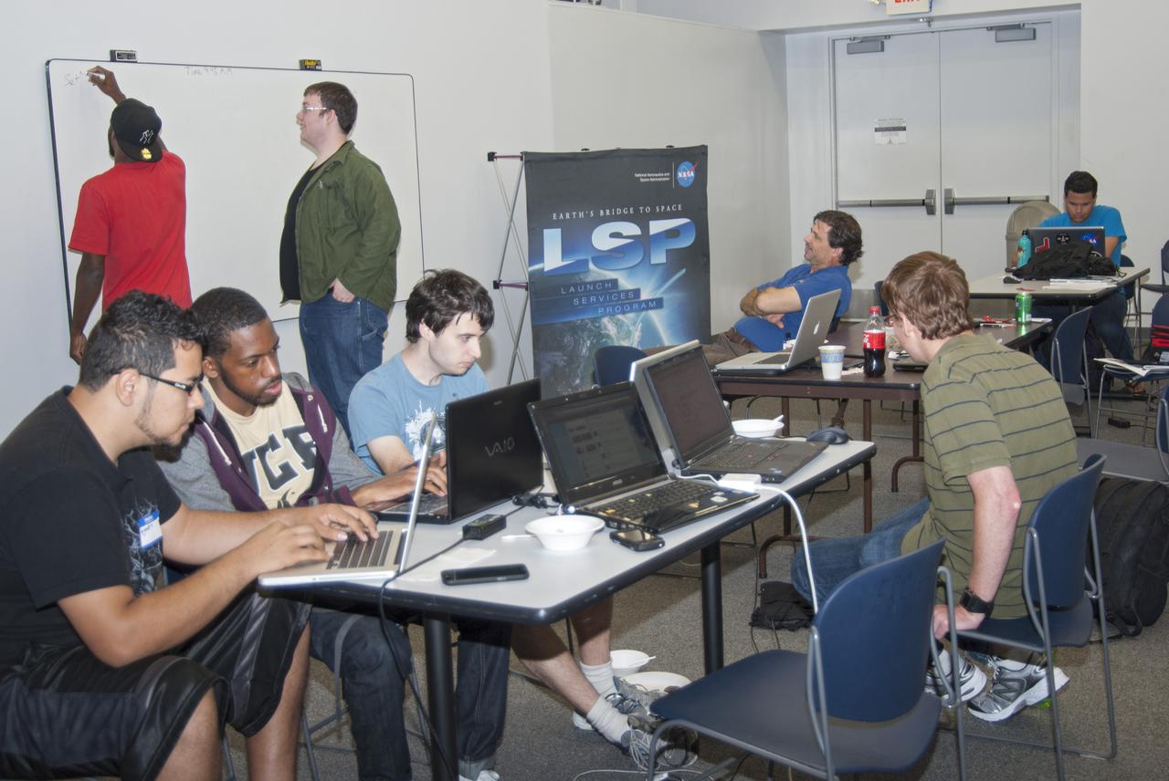 CAPE CANAVERAL, Fla. – Students from the University of Florida, the University of Central Florida, the University of Puerto Rico and private citizens brainstorm ideas during the 2013 International Space Apps Challenge, or ISAC, at The Astronaut Memorial Foundation’s Center for Space Education in Florida. Seated near the Launch Services Program poster is NASA subject matter expert Dr. Phil Metzger from Kennedy Space Center’s Swampworks Laboratory.  During the worldwide two-day challenge, more than 9,000 people and 484 organizations came together in 83 cities across 44 countries, as well as online, to develop new ways of solving challenges that NASA faces. At Kennedy, four teams brainstormed ideas with subject matter experts and others and worked nearly 32 hours straight to present their concepts to a panel of three technical and non-technical judges. Challenges tackled at Kennedy were: Deployable Greenhouse, Kennedy Space Center 2040, Seven Minutes of Science, and Moonville – Lunar Industry Game. Photo credit: NASA_Charisse Nahser