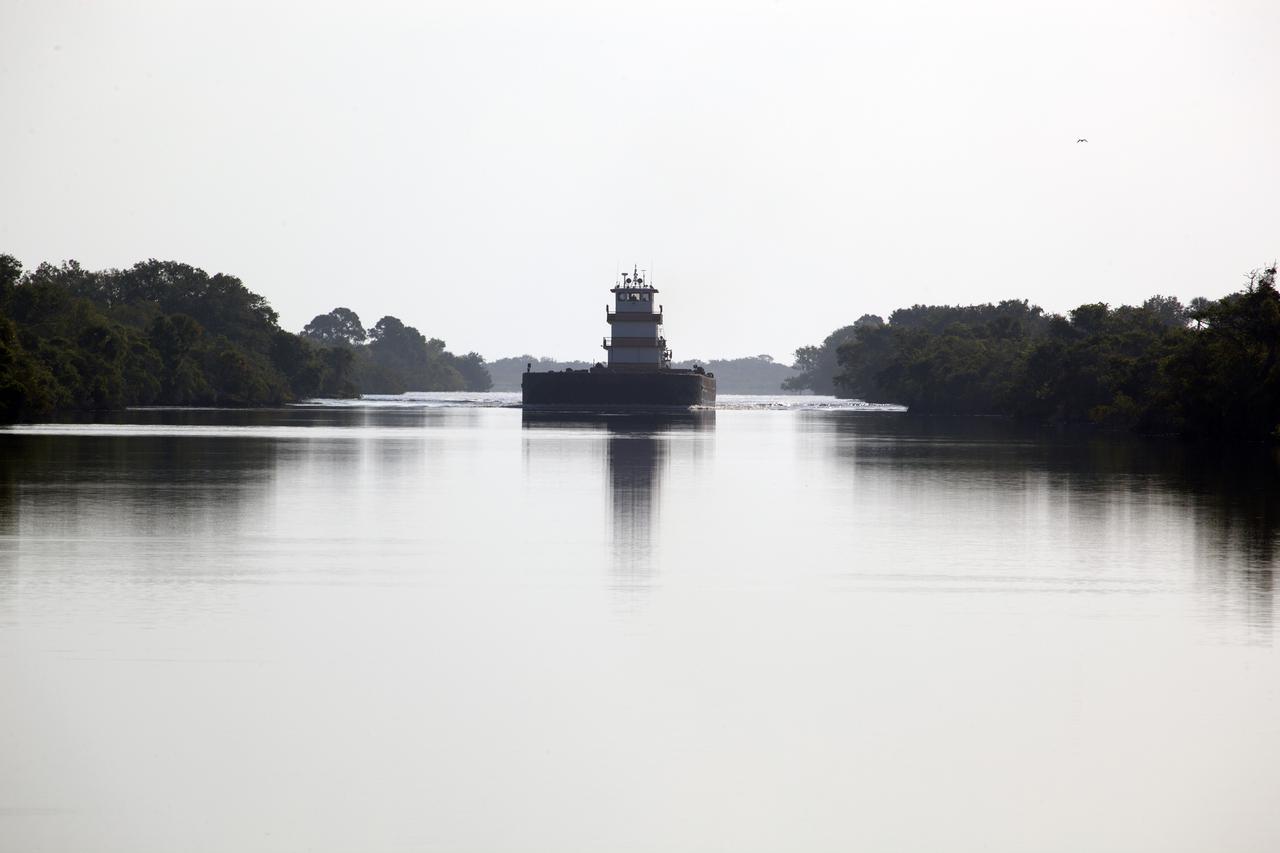 CAPE CANAVERAL, Fla. – A barge arrives at the Kennedy Space Center Turn Basin to pick up an orange flight test article space shuttle external fuel tank, or ET, an ET transporter, the crew transport vehicle, crew hatch access vehicle, solid rocket booster, or SRB, aft skirt and SRB frustum for the first leg of their journey from NASA's Kennedy Space Center in Florida to the Wings of Dreams Aviation Museum located at Keystone Heights Airport in North Central Florida.  Thousands of unique space shuttle era artifacts are being allocated to facilities across the country for their new missions to educate and inspire America's next generation of explorers. Photo credit: NASA_Dimitri Gerondidakis
