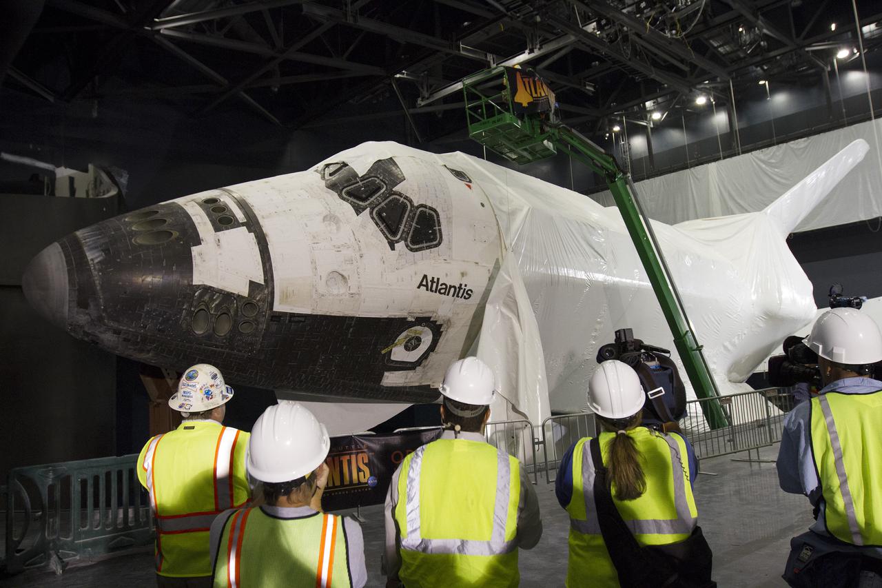 CAPE CANAVERAL, Fla. -- At the Kennedy Space Center Visitor Complex in Florida, members of the news media were on hand as construction crews begin removing 16,000 square feet of plastic shrink-wrap from the space shuttle Atlantis. The spacecraft was enclosed in the plastic shrink-wrap since November of last year to protect the artifact from dust and debris during construction of the 90,000-square-foot facility. Last November, the space shuttle Atlantis made its historic final journey to its new home, traveling 10 miles from the Kennedy Space Center's Vehicle Assembly Building to the spaceport's visitor complex. The new $100 million 'Space Shuttle Atlantis' facility will include interactive exhibits that tell the story of the 30-year Space Shuttle Program and highlights the future of space exploration. The 'Space Shuttle Atlantis' exhibit scheduled to open June 29, 2013.Photo credit: NASA_Cory Huston