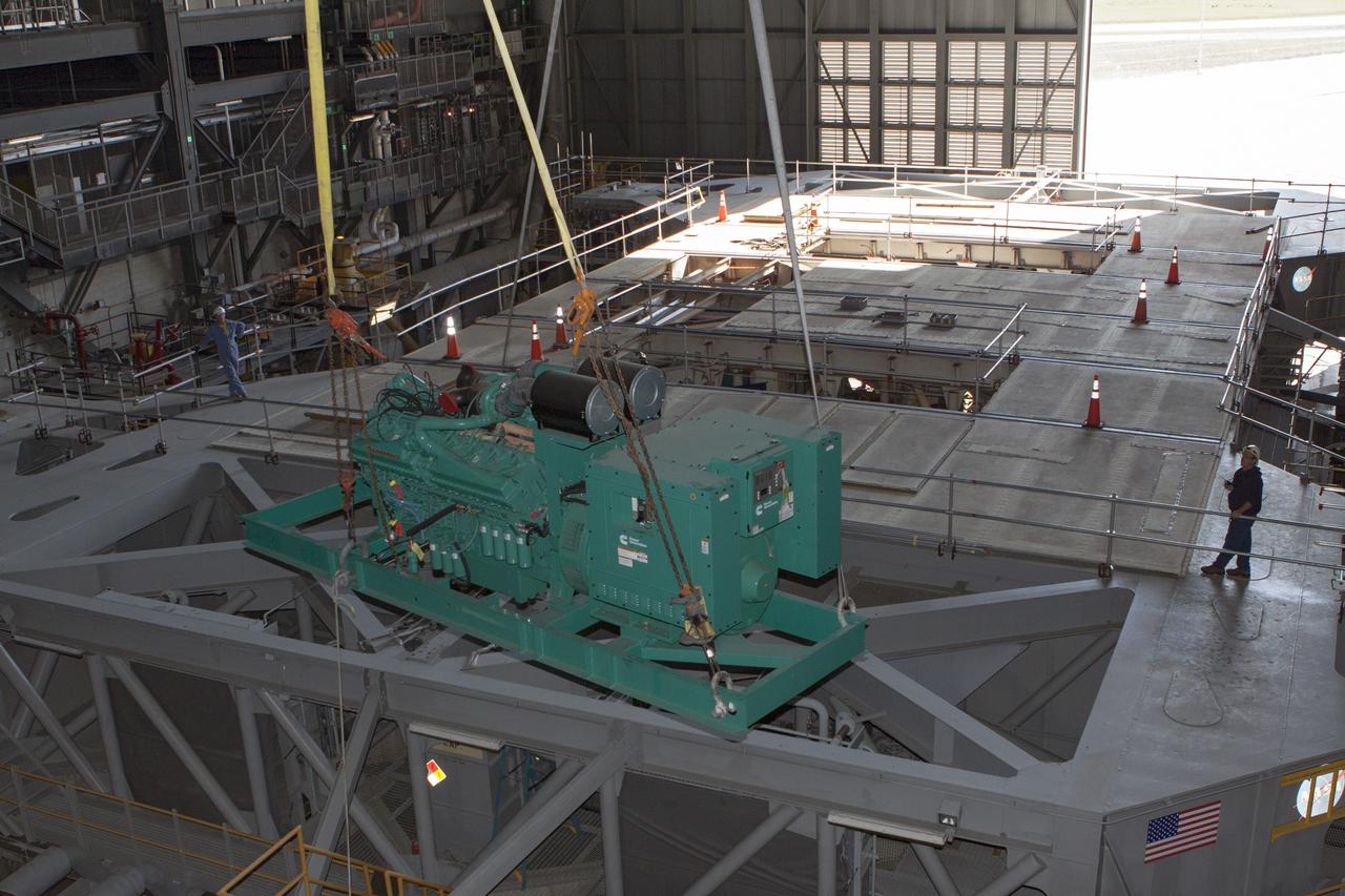 CAPE CANAVERAL, Fla. – Inside the Vehicle Assembly Building at NASA’s Kennedy Space Center in Florida, technicians monitor the progress as a large crane begins to lift a new Cummins engine and generator for installation inside crawler-transporter 1 CT-1. The Apollo era diesel engines were removed so that the new engine can be installed.  Work continues in high bay 3 to upgrade CT-1 as part of its general maintenance and could be available to carry commercial launch vehicles to the launch pad. The crawler-transporters were used to carry the mobile launcher platform and space shuttle to Launch Complex 39 for space shuttle launches for 30 years.  Photo credit: NASA_Kim Shiflett