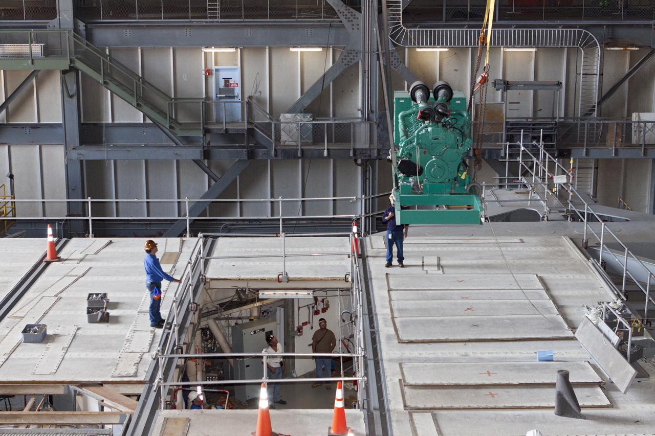 CAPE CANAVERAL, Fla. – Inside the Vehicle Assembly Building at NASA’s Kennedy Space Center in Florida, technicians monitor the progress as a large crane is used to lift a new Cummins engine and generator for installation inside crawler-transporter 1 CT-1. The Apollo era diesel engines were removed so that the new engine can be installed.  Work continues in high bay 3 to upgrade CT-1 as part of its general maintenance and could be available to carry commercial launch vehicles to the launch pad. The crawler-transporters were used to carry the mobile launcher platform and space shuttle to Launch Complex 39 for space shuttle launches for 30 years.  Photo credit: NASA_Kim Shiflett