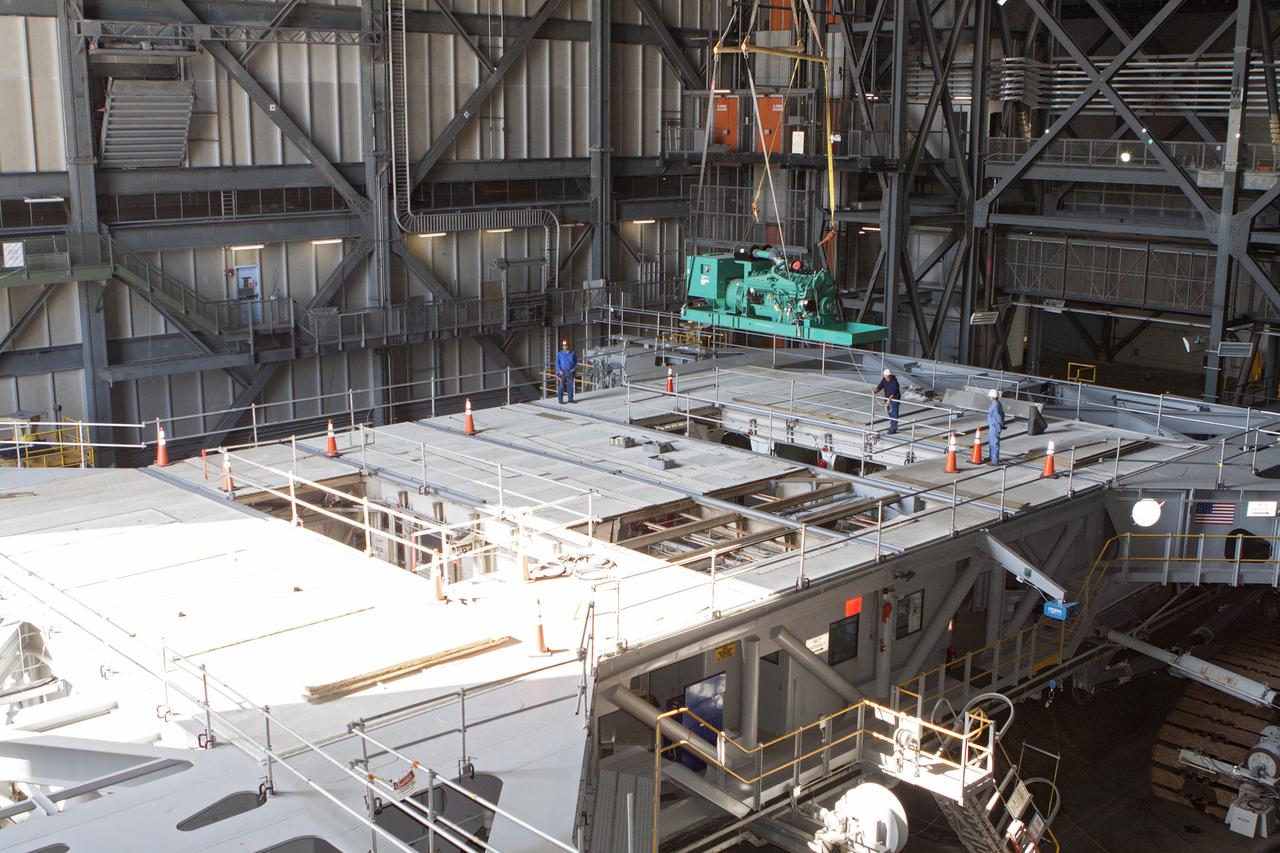CAPE CANAVERAL, Fla. – Inside the Vehicle Assembly Building at NASA’s Kennedy Space Center in Florida, technicians monitor the progress as a large crane lifts a new Cummins engine and generator for installation inside crawler-transporter 1 CT-1. The Apollo era diesel engines were removed so that the new engine can be installed.  Work continues in high bay 3 to upgrade CT-1 as part of its general maintenance and could be available to carry commercial launch vehicles to the launch pad. The crawler-transporters were used to carry the mobile launcher platform and space shuttle to Launch Complex 39 for space shuttle launches for 30 years.  Photo credit: NASA_Kim Shiflett