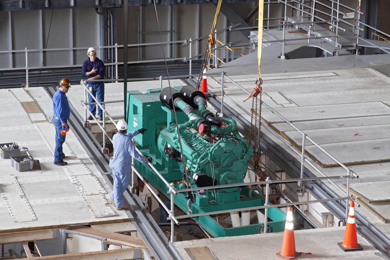 CAPE CANAVERAL, Fla. – Inside the Vehicle Assembly Building at NASA’s Kennedy Space Center in Florida, technicians monitor the progress as a large crane is used to lower a new Cummins engine and generator for installation inside crawler-transporter 1 CT-1. The Apollo era diesel engines were removed so that the new engine can be installed.   Work continues in high bay 3 to upgrade CT-1 as part of its general maintenance and could be available to carry commercial launch vehicles to the launch pad. The crawler-transporters were used to carry the mobile launcher platform and space shuttle to Launch Complex 39 for space shuttle launches for 30 years.  Photo credit: NASA_Kim Shiflett