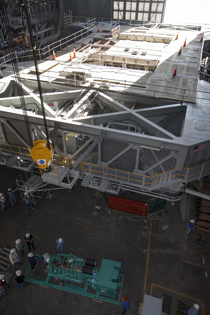 CAPE CANAVERAL, Fla. – Inside the Vehicle Assembly Building at NASA’s Kennedy Space Center in Florida, a large crane is lowered toward a new Cummins engine and generator that is being prepared for installation inside crawler-transporter 1 CT-1. The Apollo era diesel engines were removed so that the new engine could be installed.    Work continues in high bay 3 to upgrade CT-1 as part of its general maintenance and could be available to carry commercial launch vehicles to the launch pad. The crawler-transporters were used to carry the mobile launcher platform and space shuttle to Launch Complex 39 for space shuttle launches for 30 years.  Photo credit: NASA_Kim Shiflett