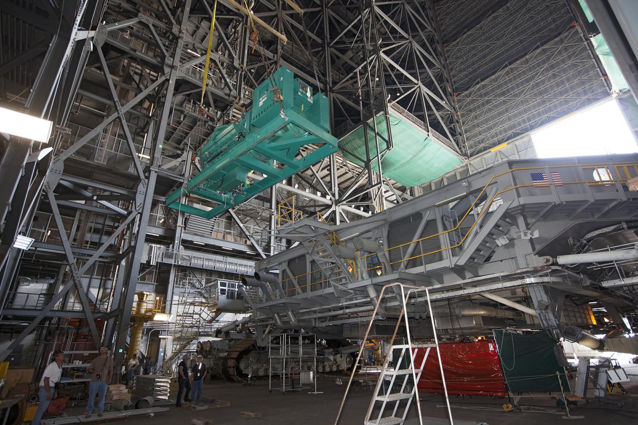 CAPE CANAVERAL, Fla. – Inside the Vehicle Assembly Building at NASA’s Kennedy Space Center in Florida, technicians monitor the progress as a large crane lifts a new Cummins engine and generator high above crawler-transporter 1 CT-1. The Apollo era diesel engines were removed so that the new engine can be installed inside CT-1.     Work continues in high bay 3 to upgrade CT-1 as part of its general maintenance and could be available to carry commercial launch vehicles to the launch pad. The crawler-transporters were used to carry the mobile launcher platform and space shuttle to Launch Complex 39 for space shuttle launches for 30 years.  Photo credit: NASA_Kim Shiflett